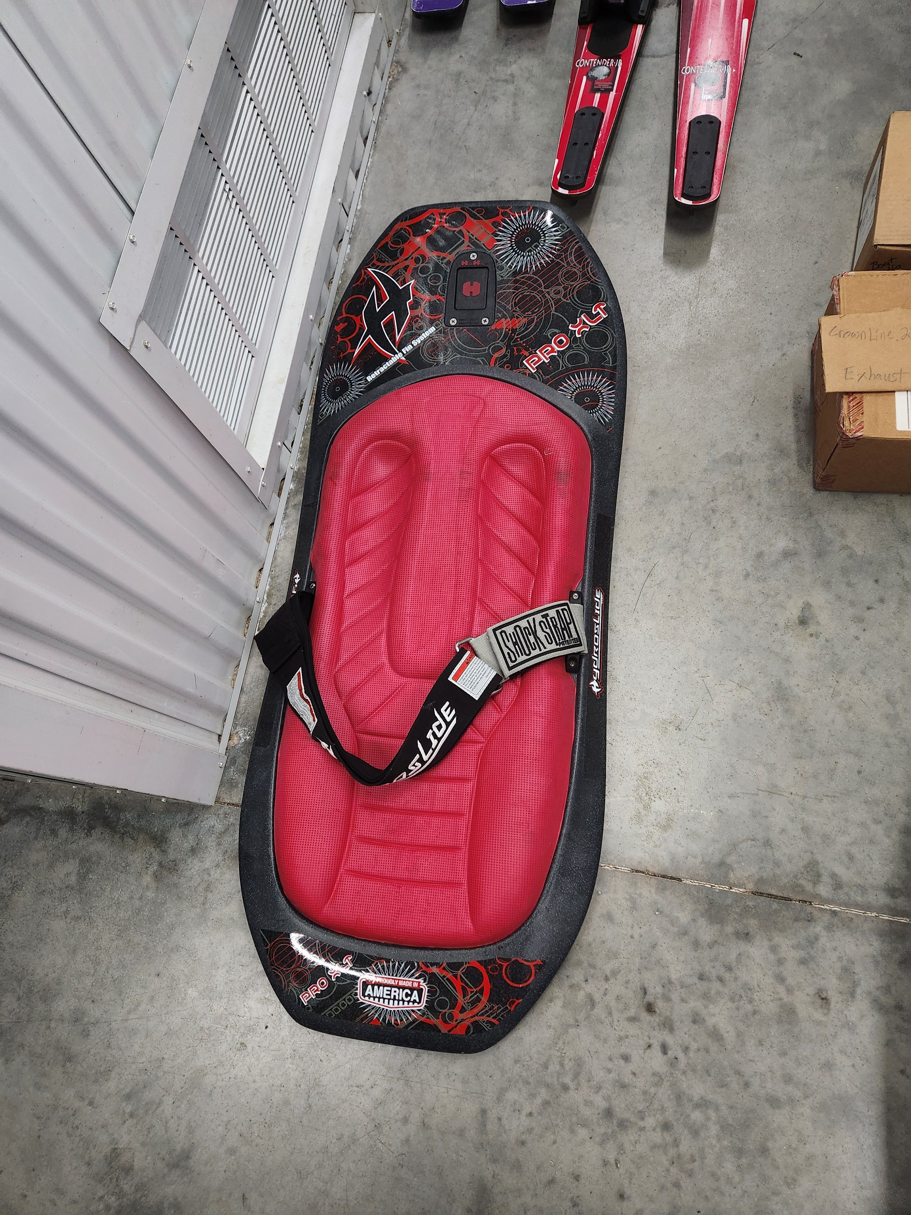 Red kneeboard on concrete floor next to water skis.