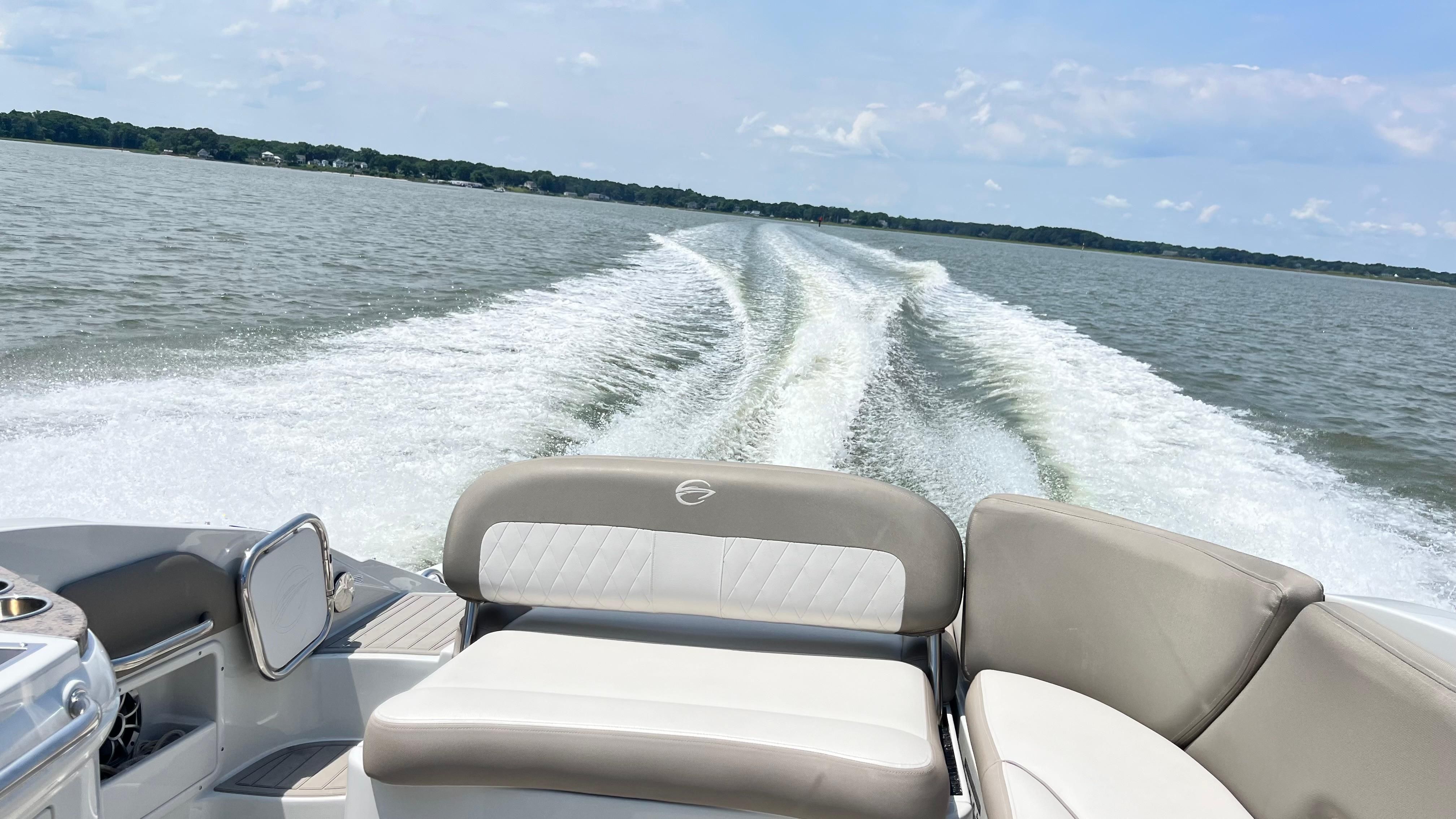The image shows the stern of a Crownline E 285 boat on the water with a wake behind.