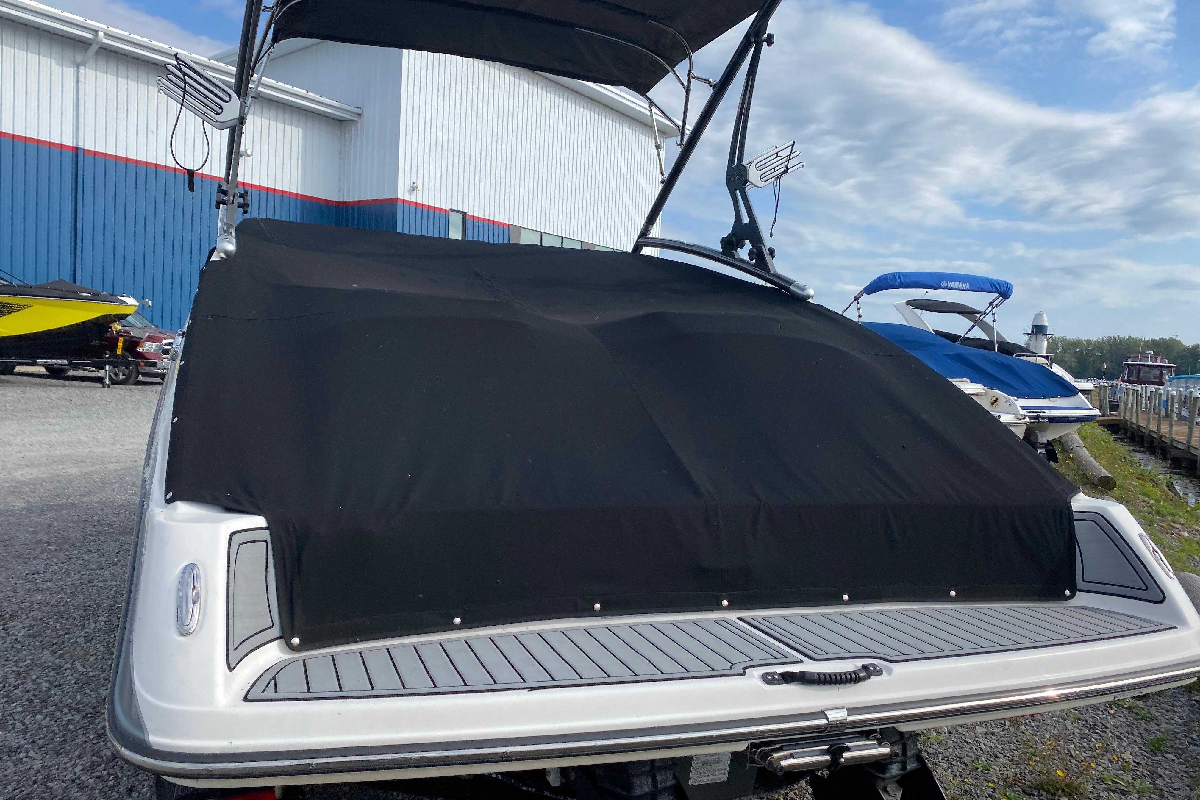 2015 Yamaha Boats 212X with black cover, docked near blue and white buildings.