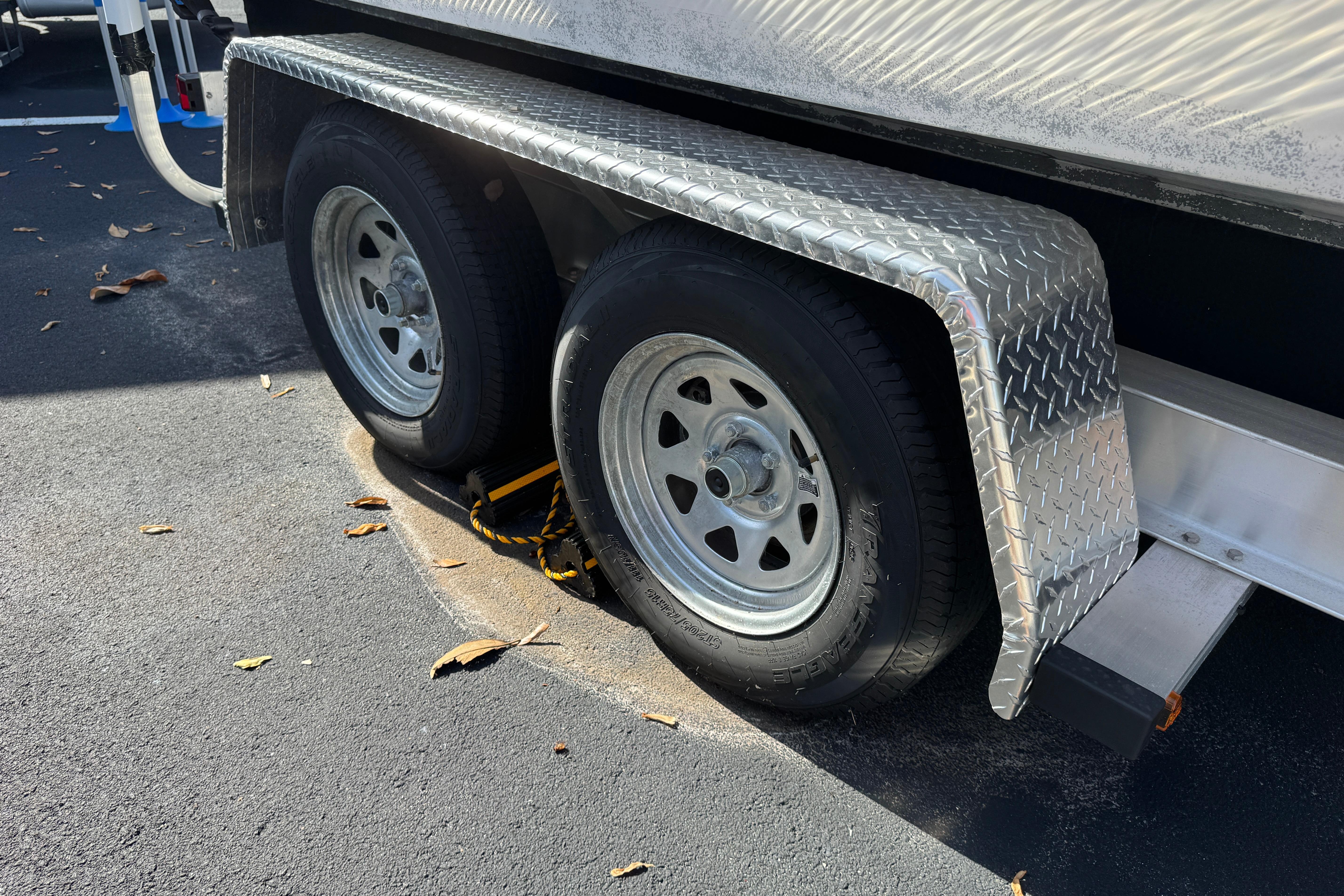 Trailer wheels of a 2018 Hurricane SunDeck 2400 OB, parked on asphalt with metal fenders.