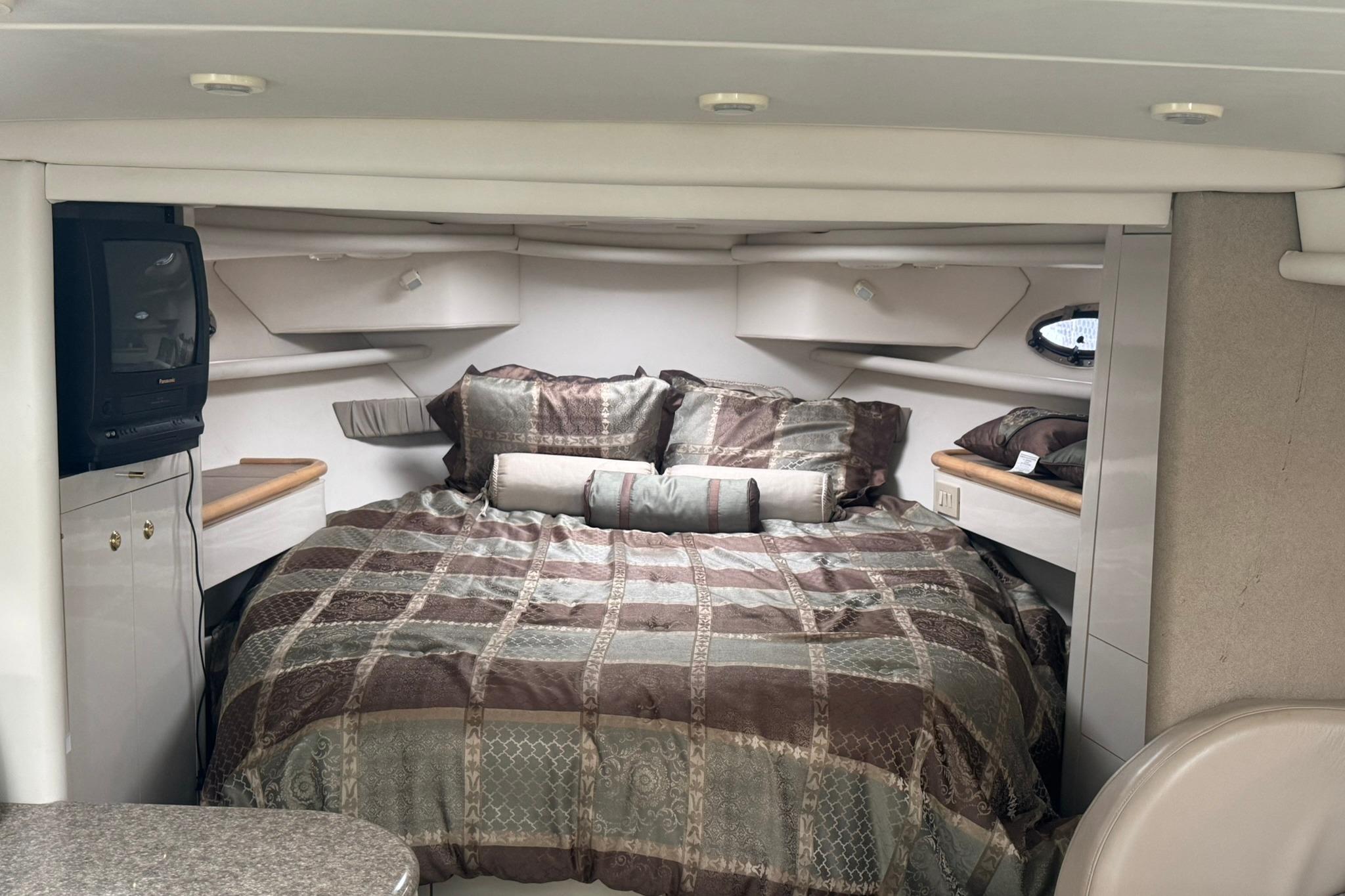 1998 Maxum 3700 SCR cabin interior with cozy bed and vintage TV setup.