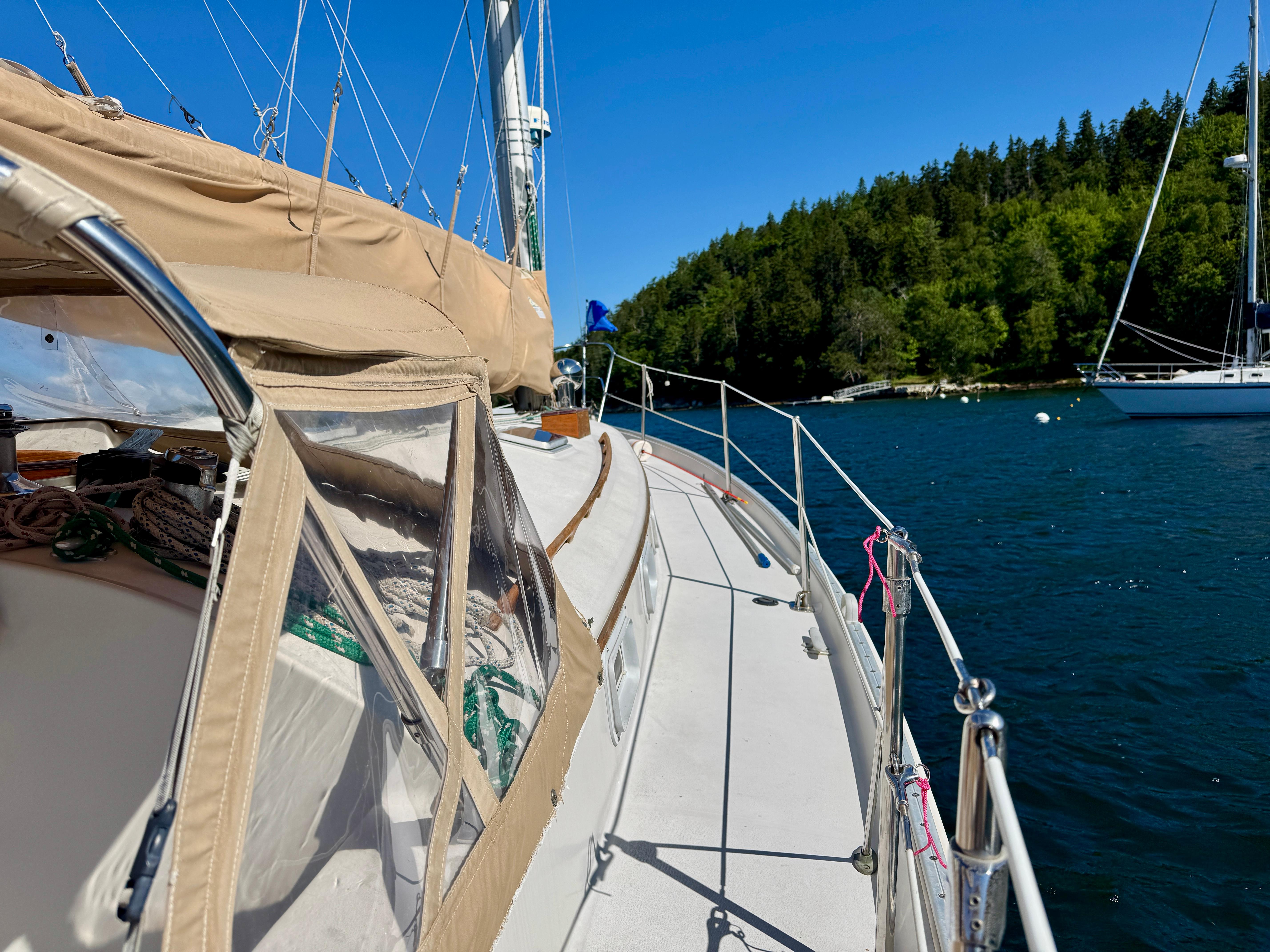 1989 Nonsuch 30 Ultra sailboat on serene water near lush green shoreline.