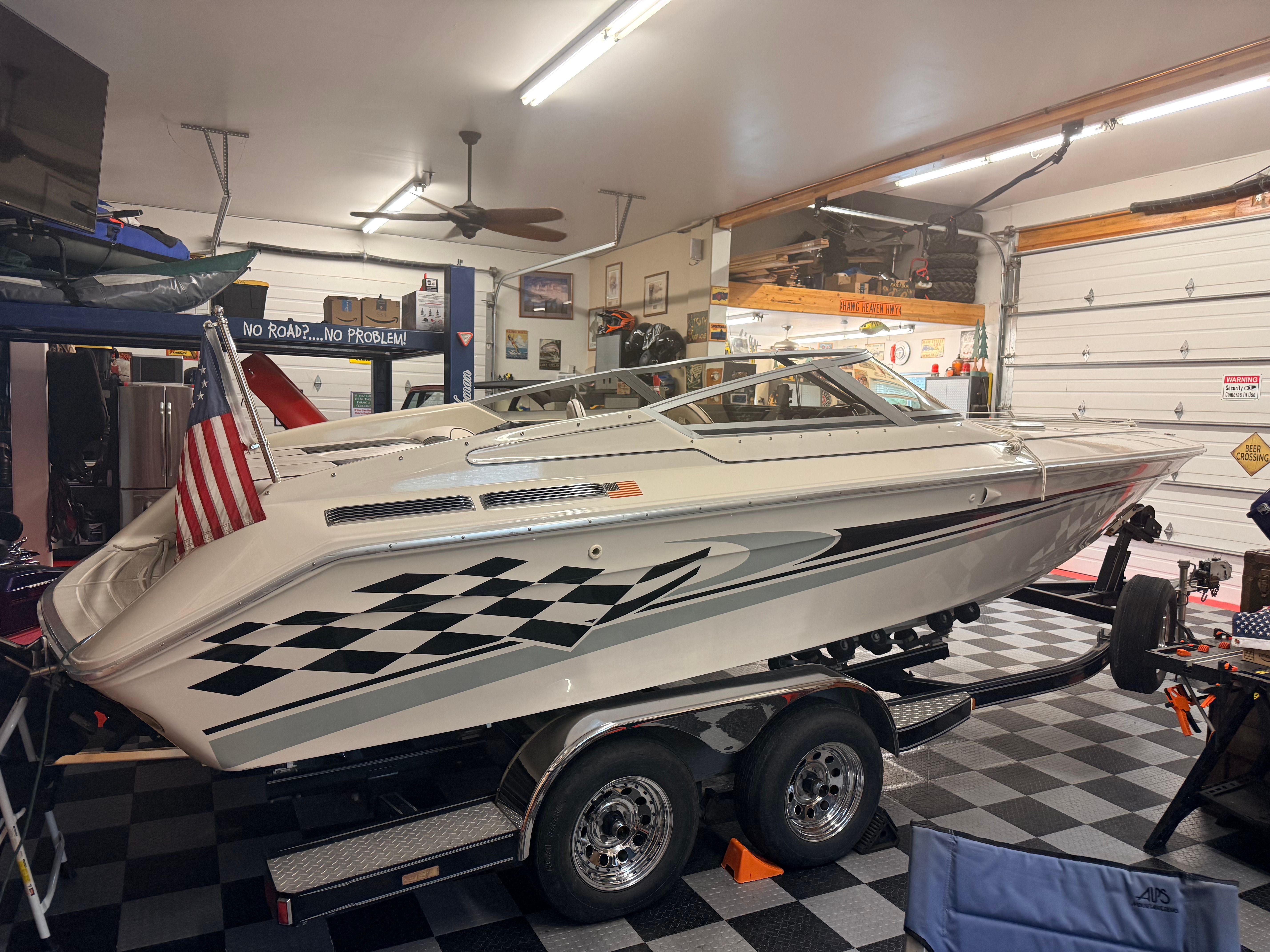 A white motorboat with a checkered pattern sits in a garage on a trailer.