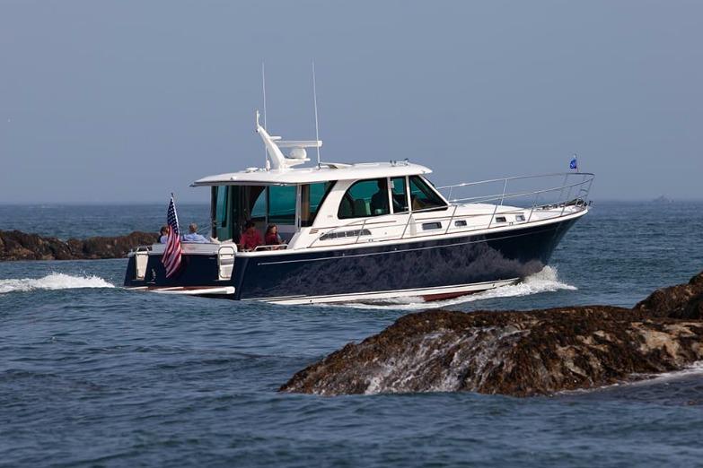 2026 Sabre 45 Salon Express cruising near rocky shoreline.