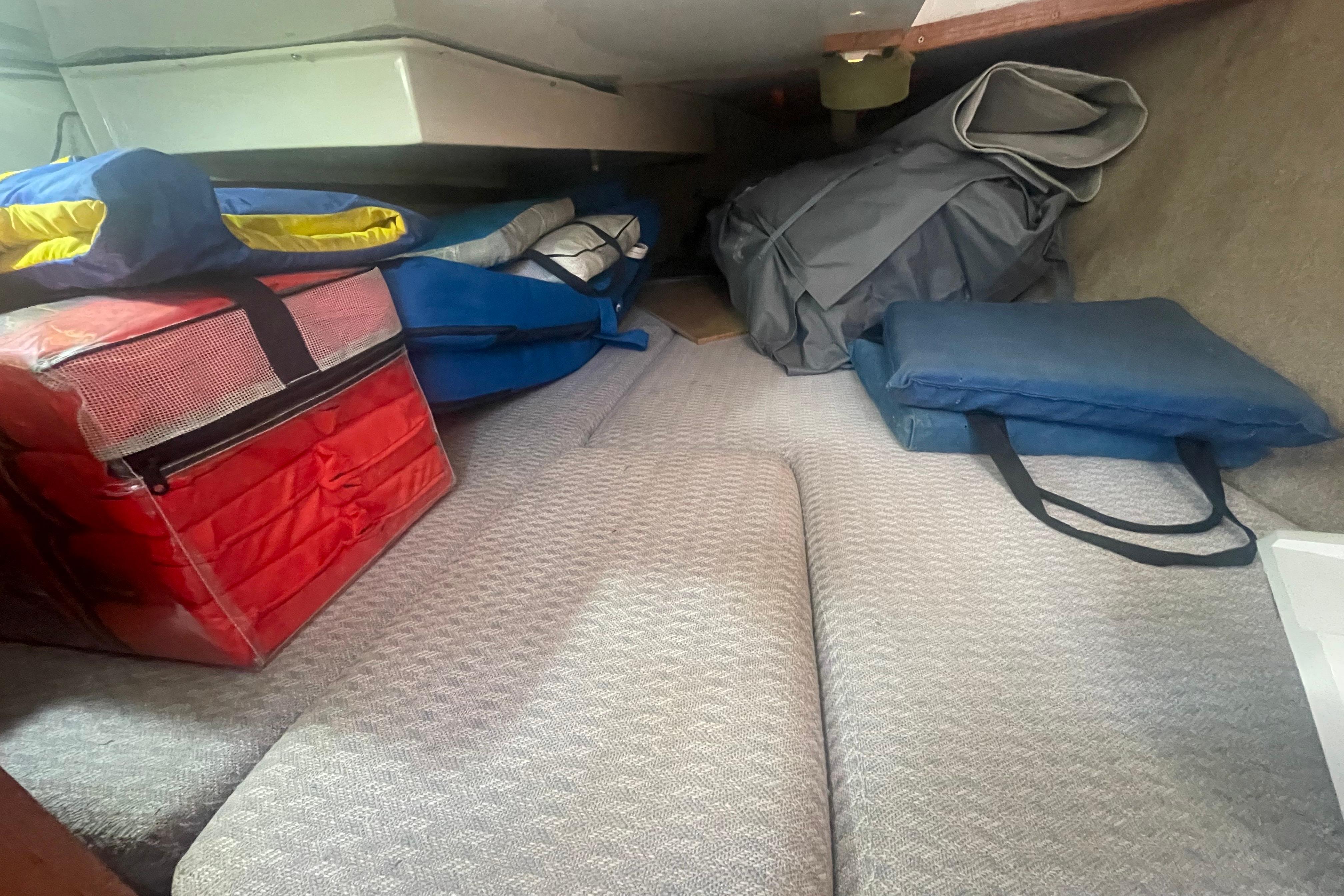 Interior storage area of a 1987 Beneteau 31 sailboat with various bags and cushions.