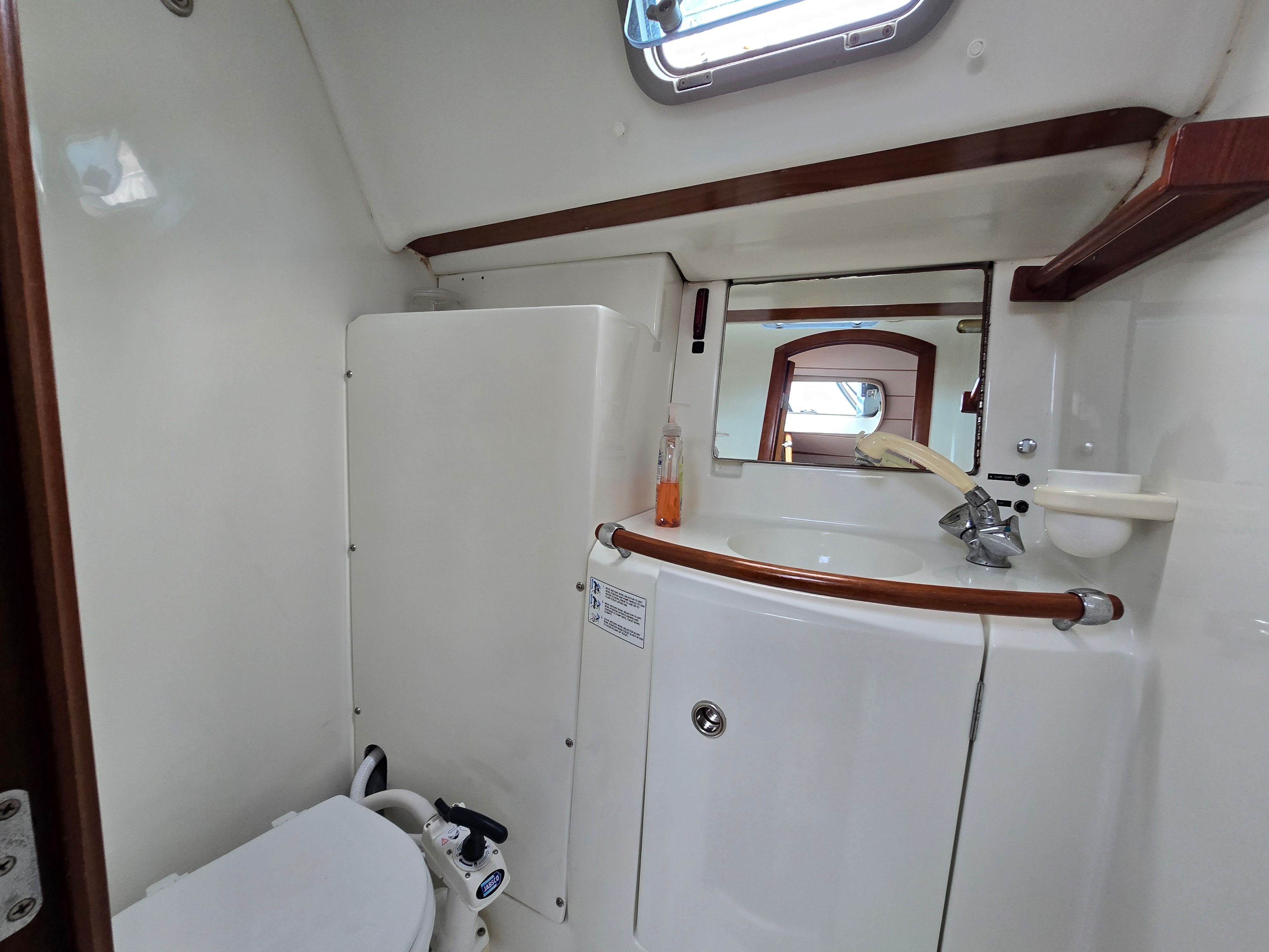 Interior view of a boat bathroom with toilet, sink, and mirror.