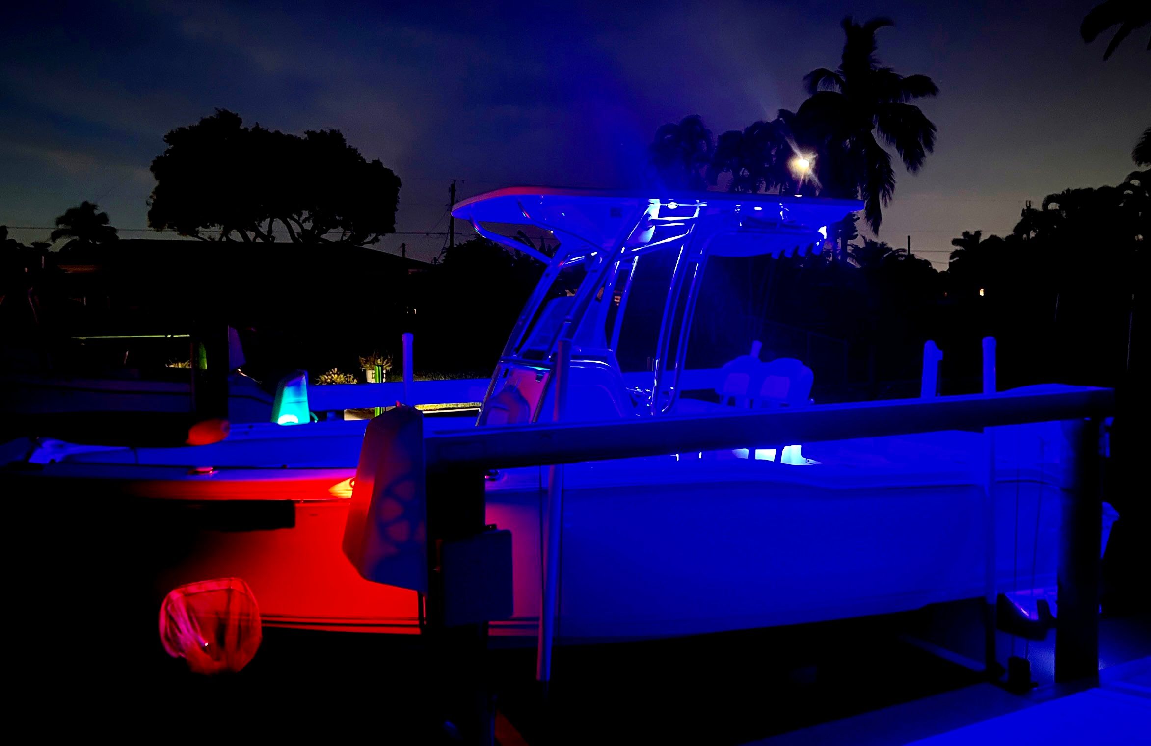 A boat illuminated in the dark, surrounded by trees and a calm water backdrop.