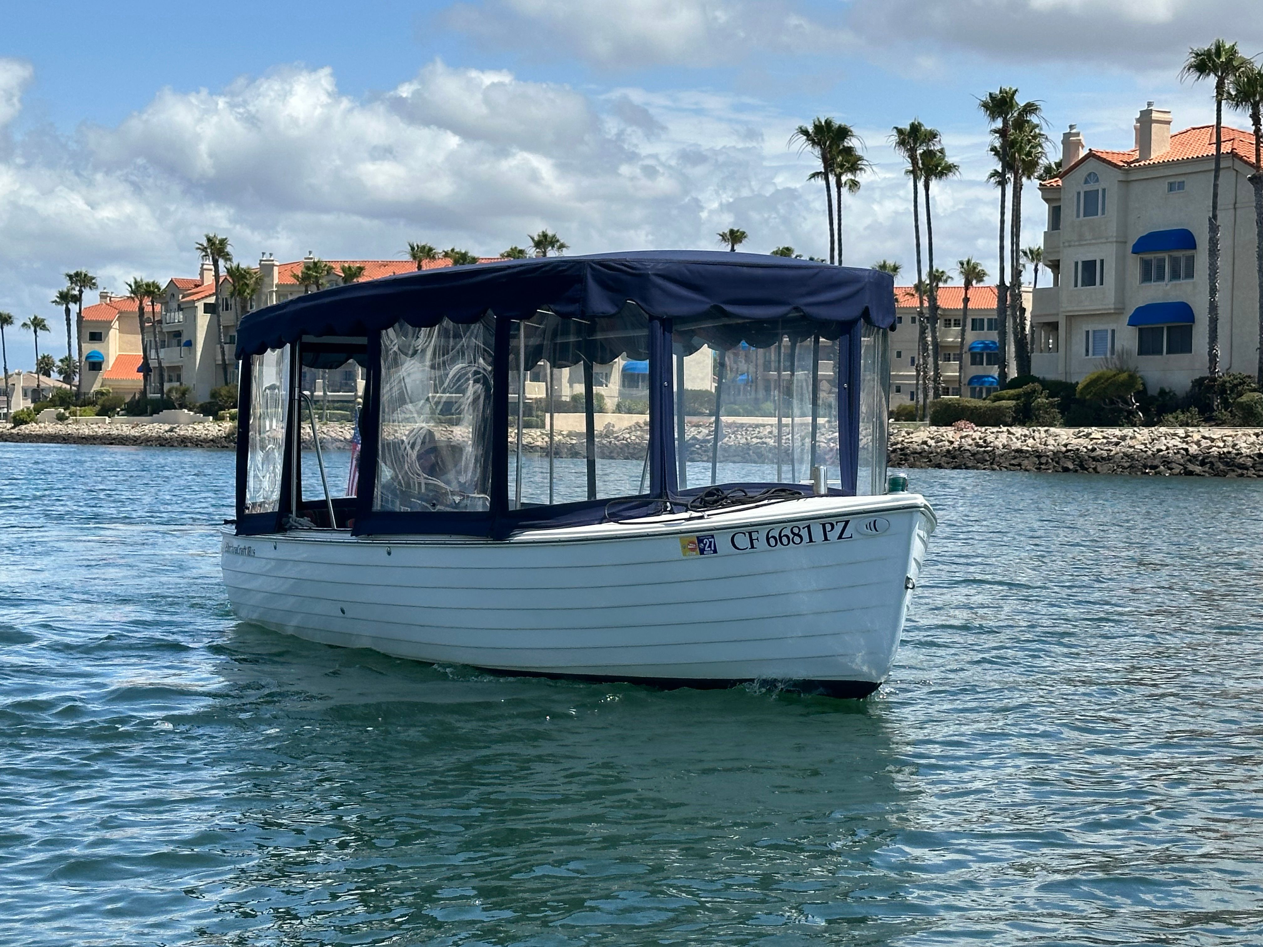 A white boat with a blue canopy navigates calm waters near a coastal backdrop.