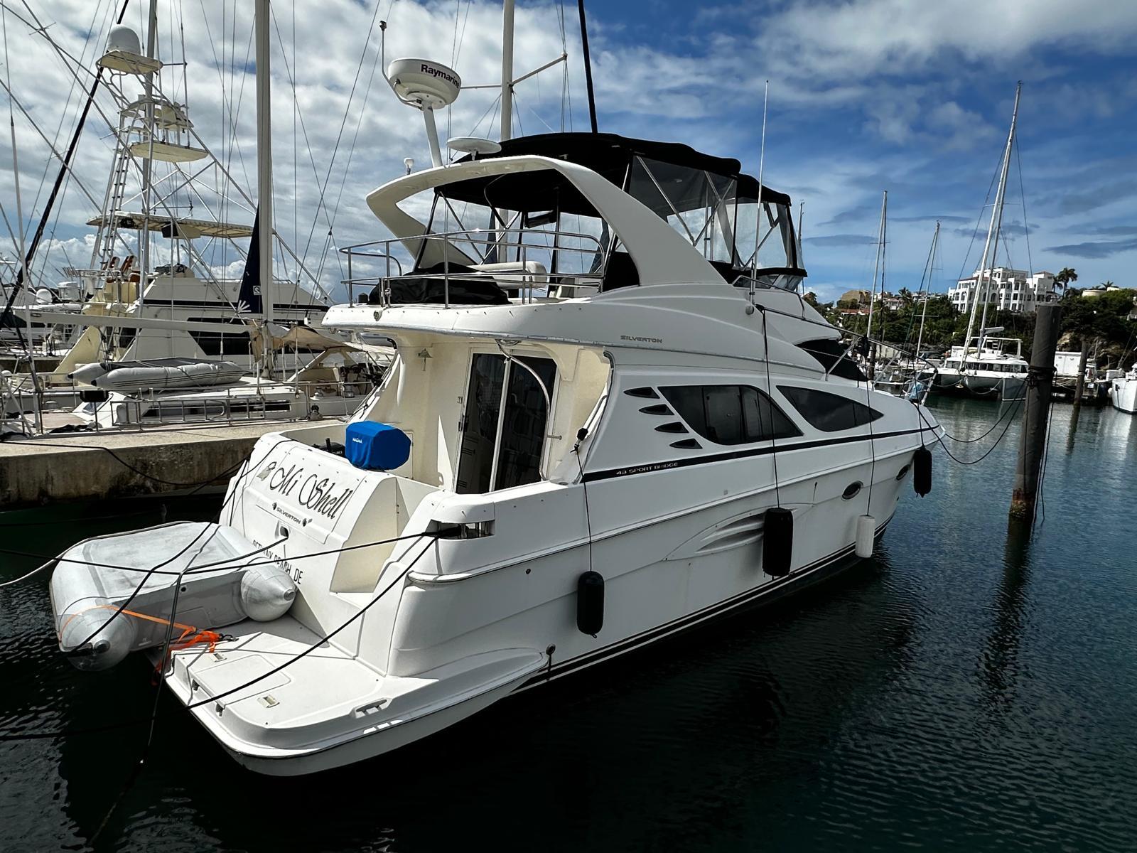 2006 Silverton 43 Sport Bridge yacht docked in a marina under a partly cloudy sky.