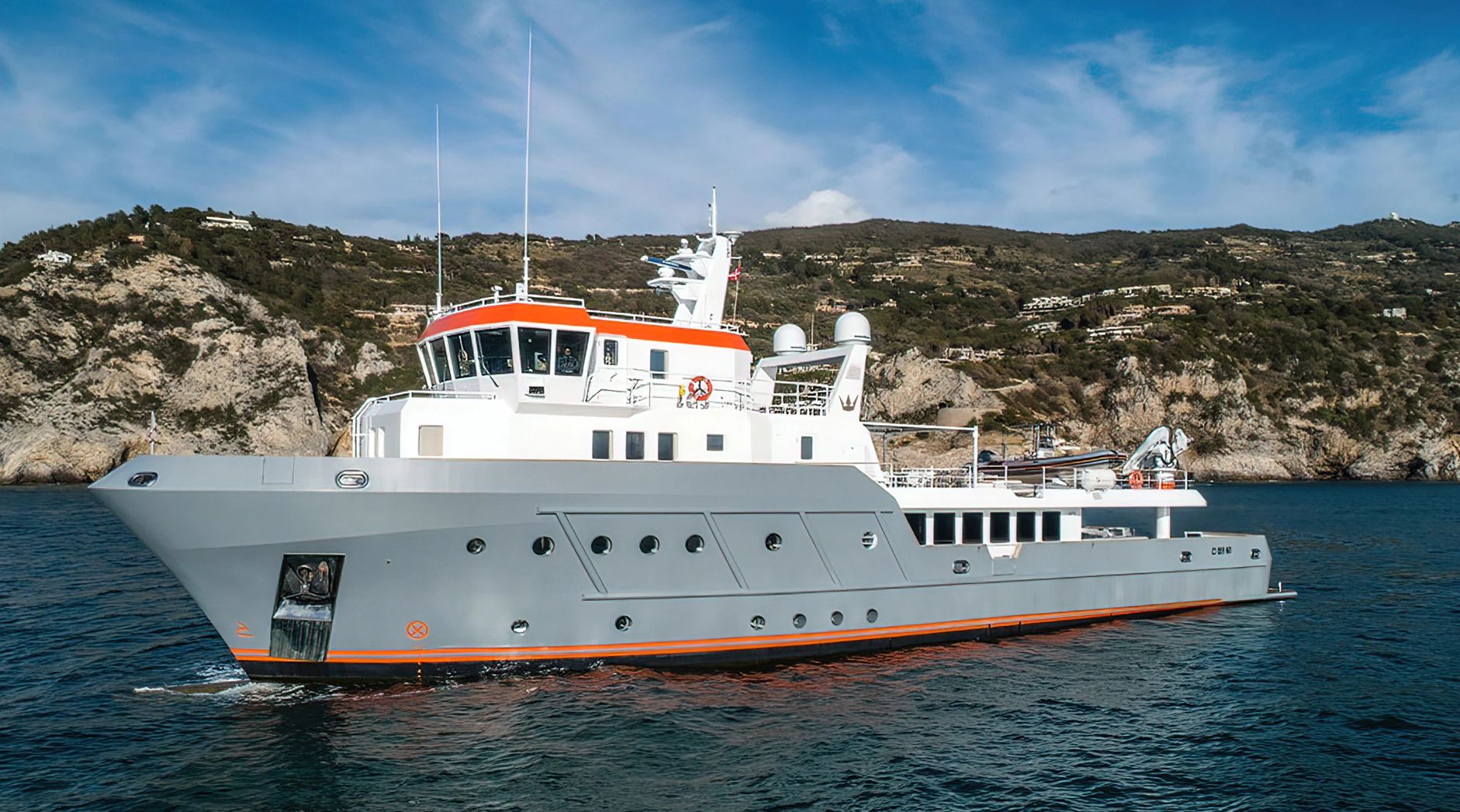 Ocean King Explorer 130 yacht from 2028 on the water near a rocky coastline.