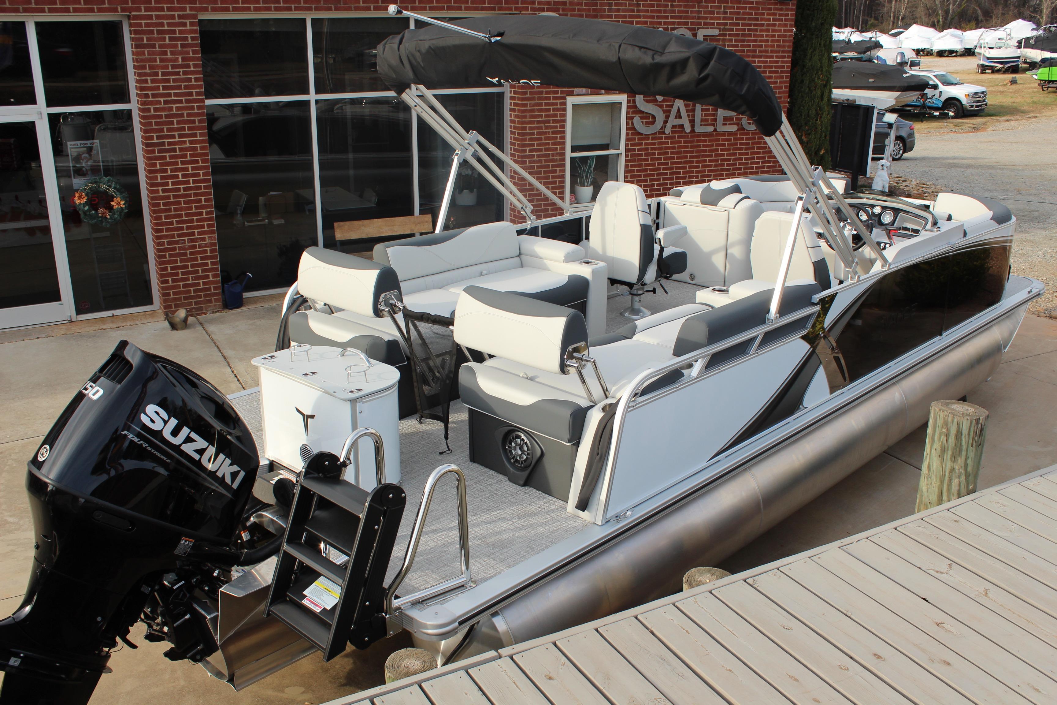 2026 Tahoe Pontoon LTZ boat with Suzuki engine, docked near a brick building.
