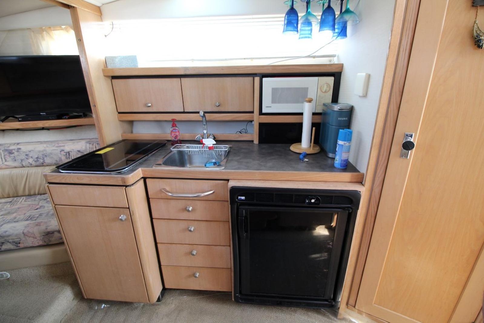 1999 Bayliner 3255 Avanti boat interior kitchen with sink, stove, microwave, and fridge.