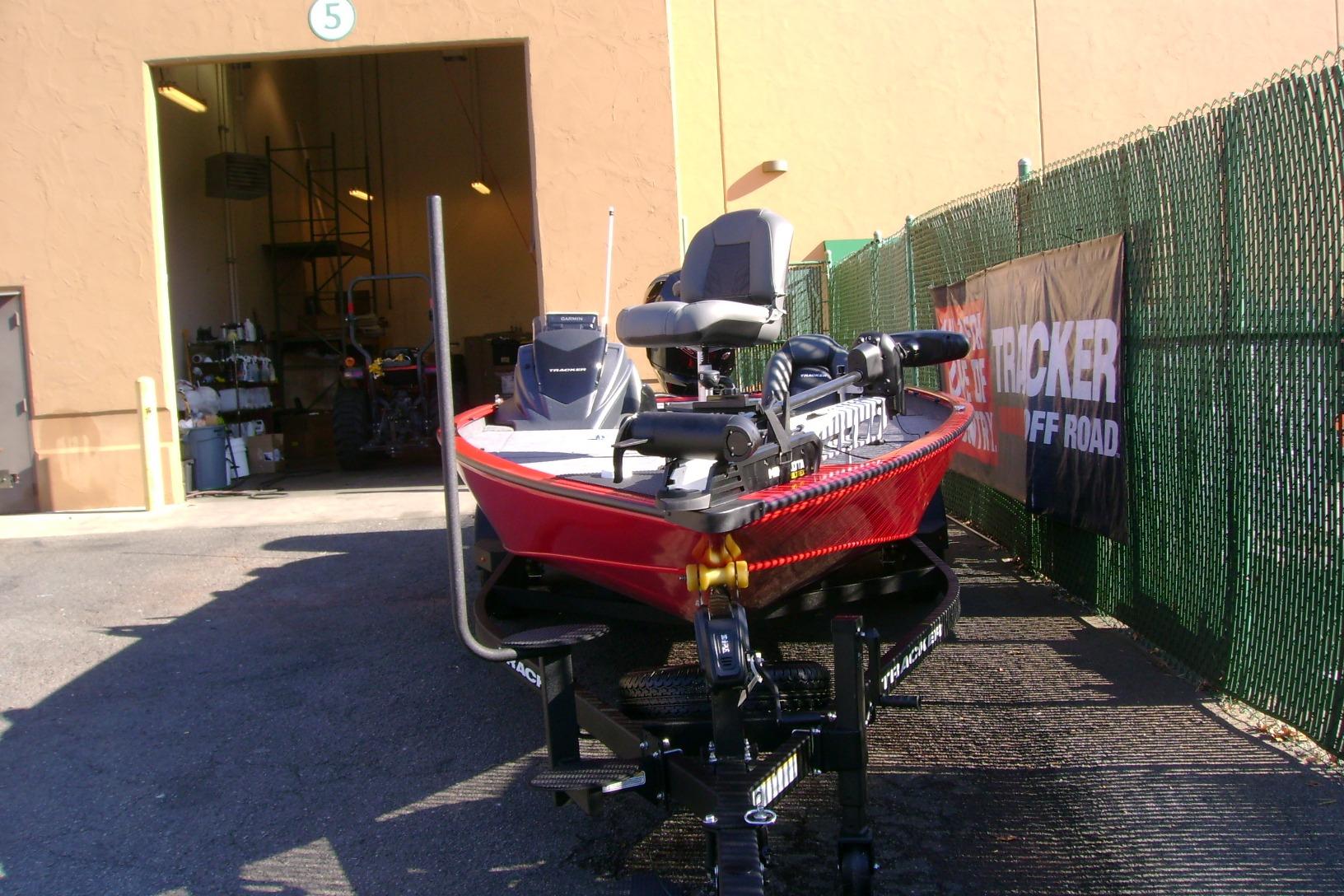 2026 Tracker Savage 215 boat in red, parked outside a garage with equipment.