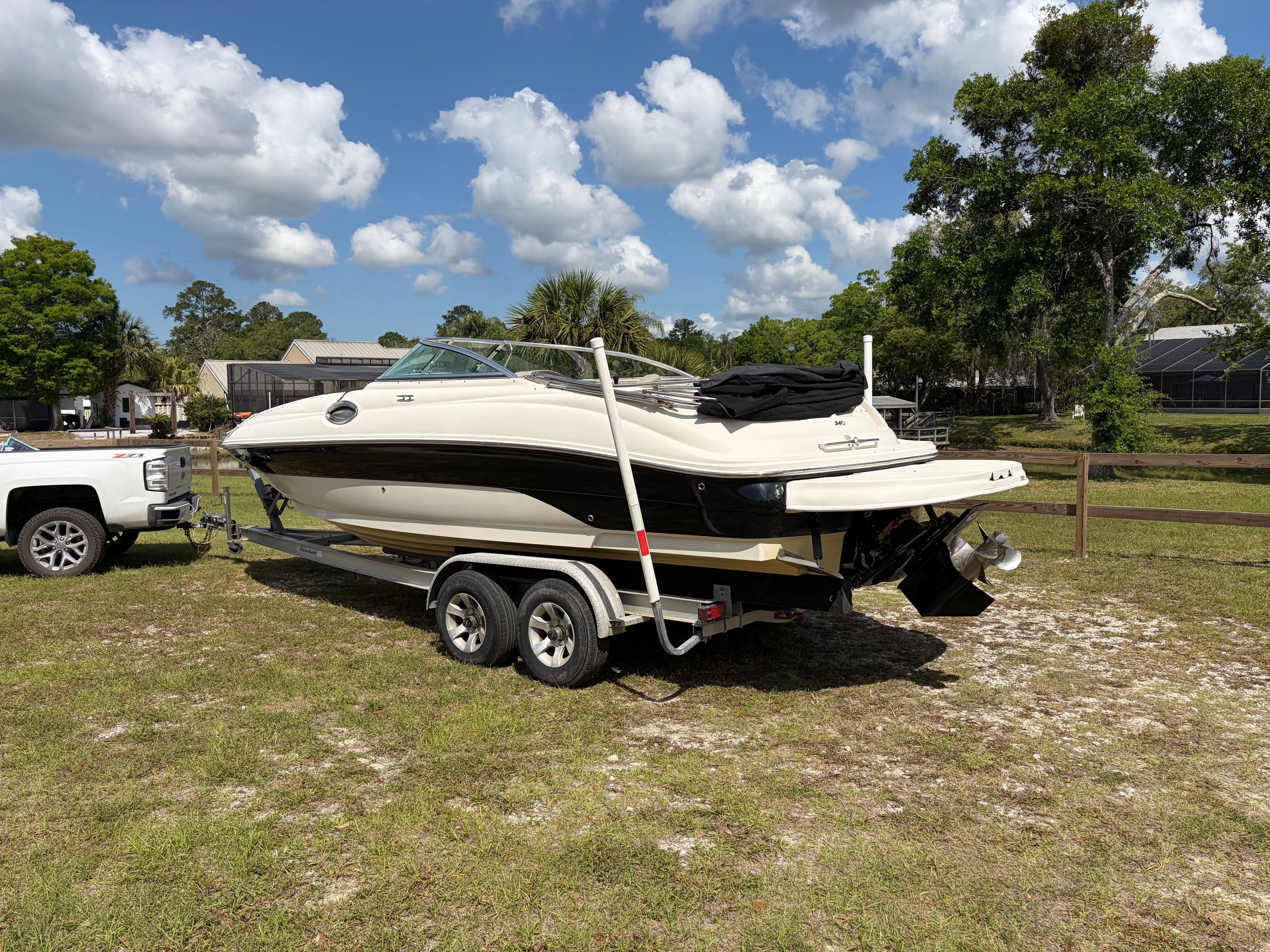A white and black bowrider boat on a trailer, parked on grass under a blue sky.