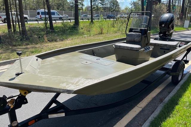 2026 Tracker Grizzly 1860 CC boat on trailer, parked outdoors near trees and road.