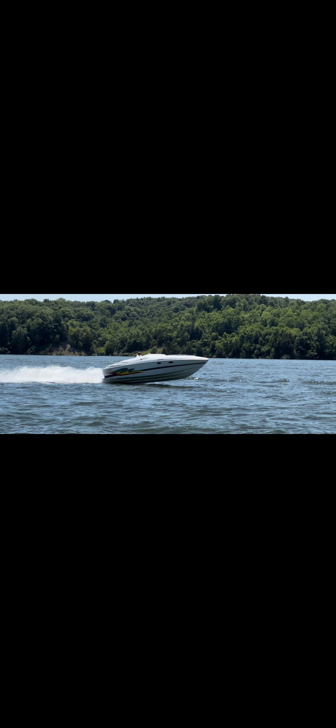 A 1996 Baja 302 Boss speeding across the water, surrounded by green trees.
