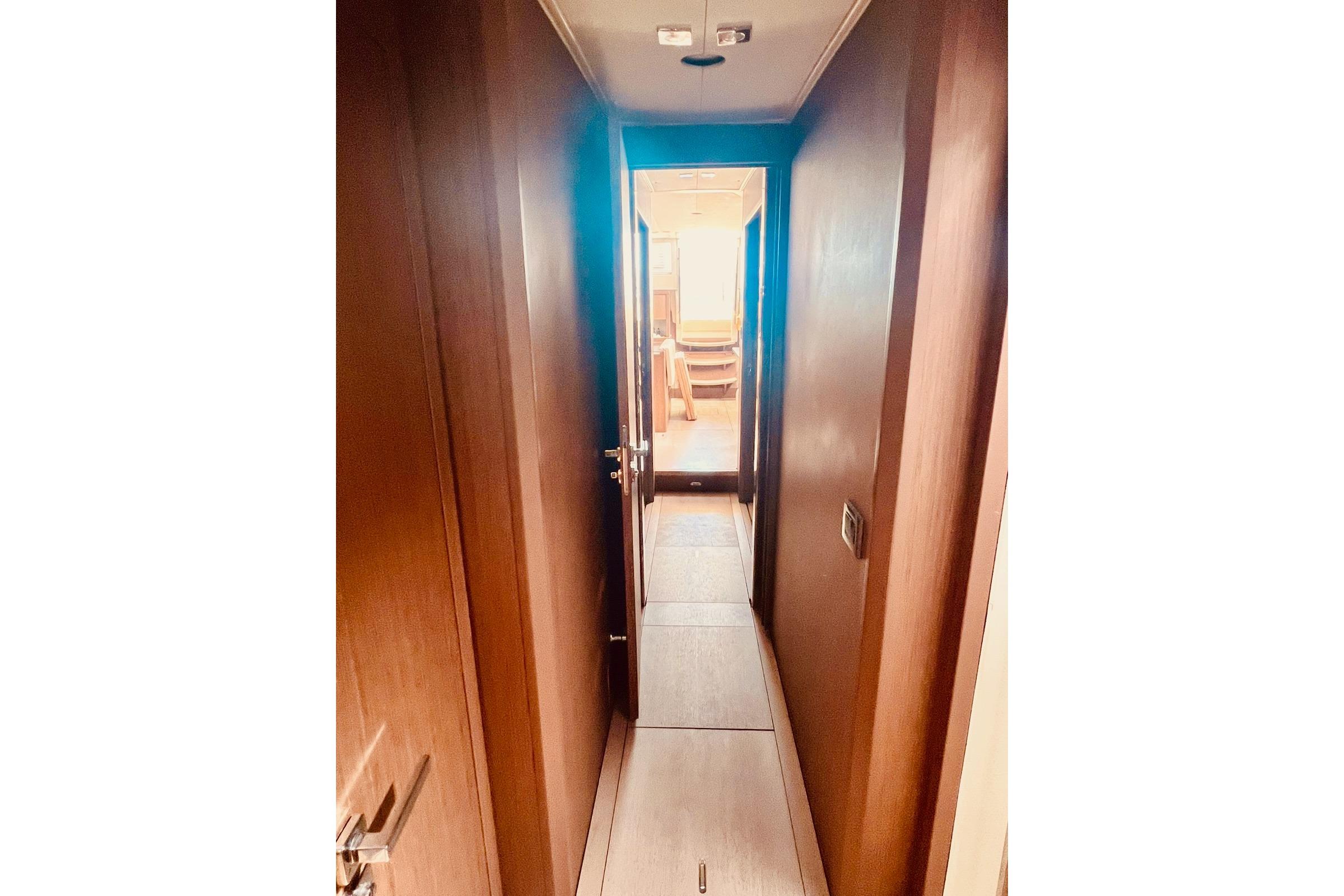 Narrow hallway inside 2017 Beneteau Sense 57 yacht, featuring wooden walls and flooring.
