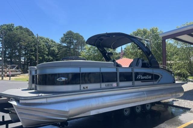 2024 Manitou 25 LX SRW pontoon boat on trailer, parked outdoors.