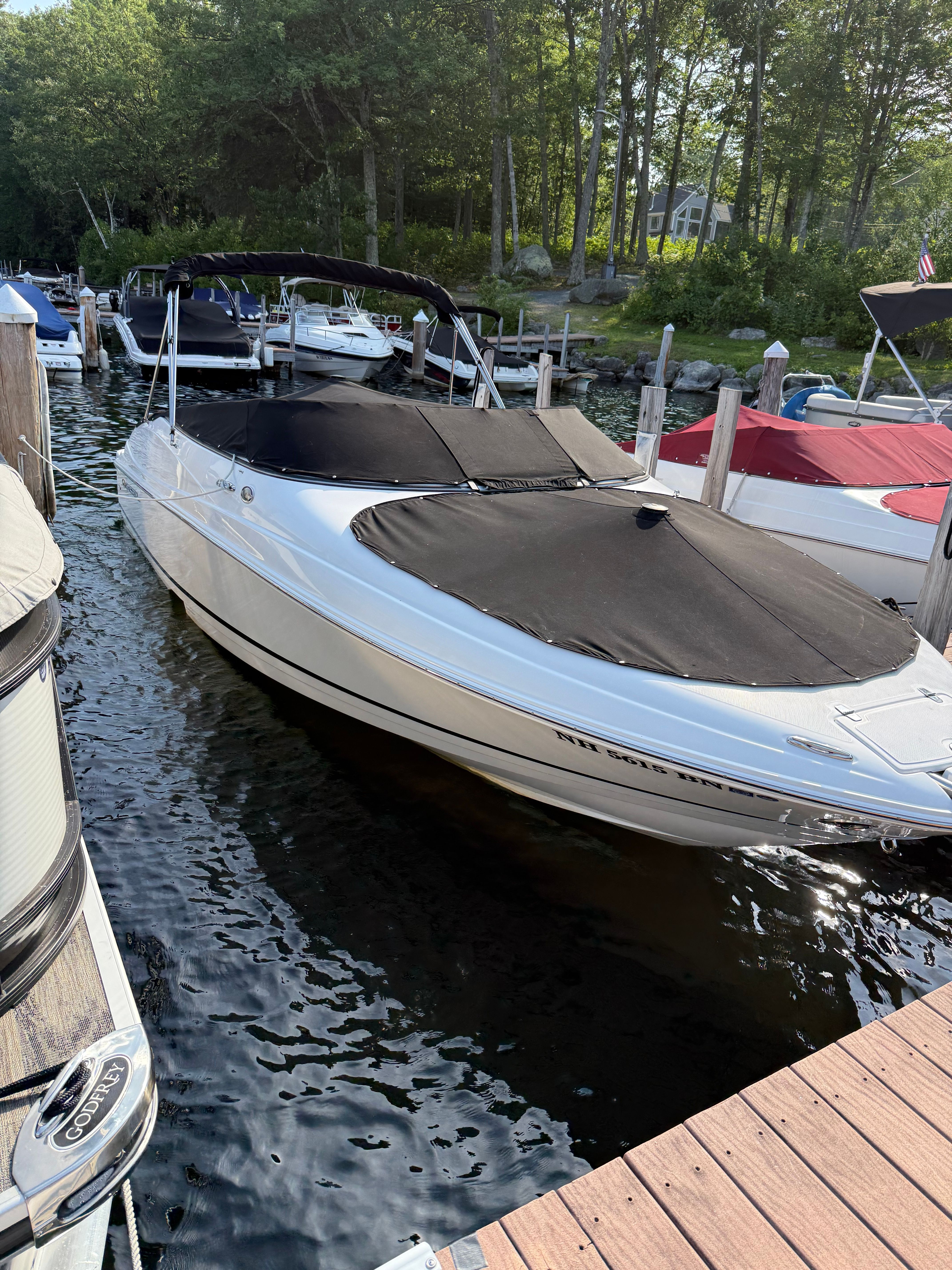 2007 Regal 2400 Bowrider boat docked with black covers, surrounded by trees.