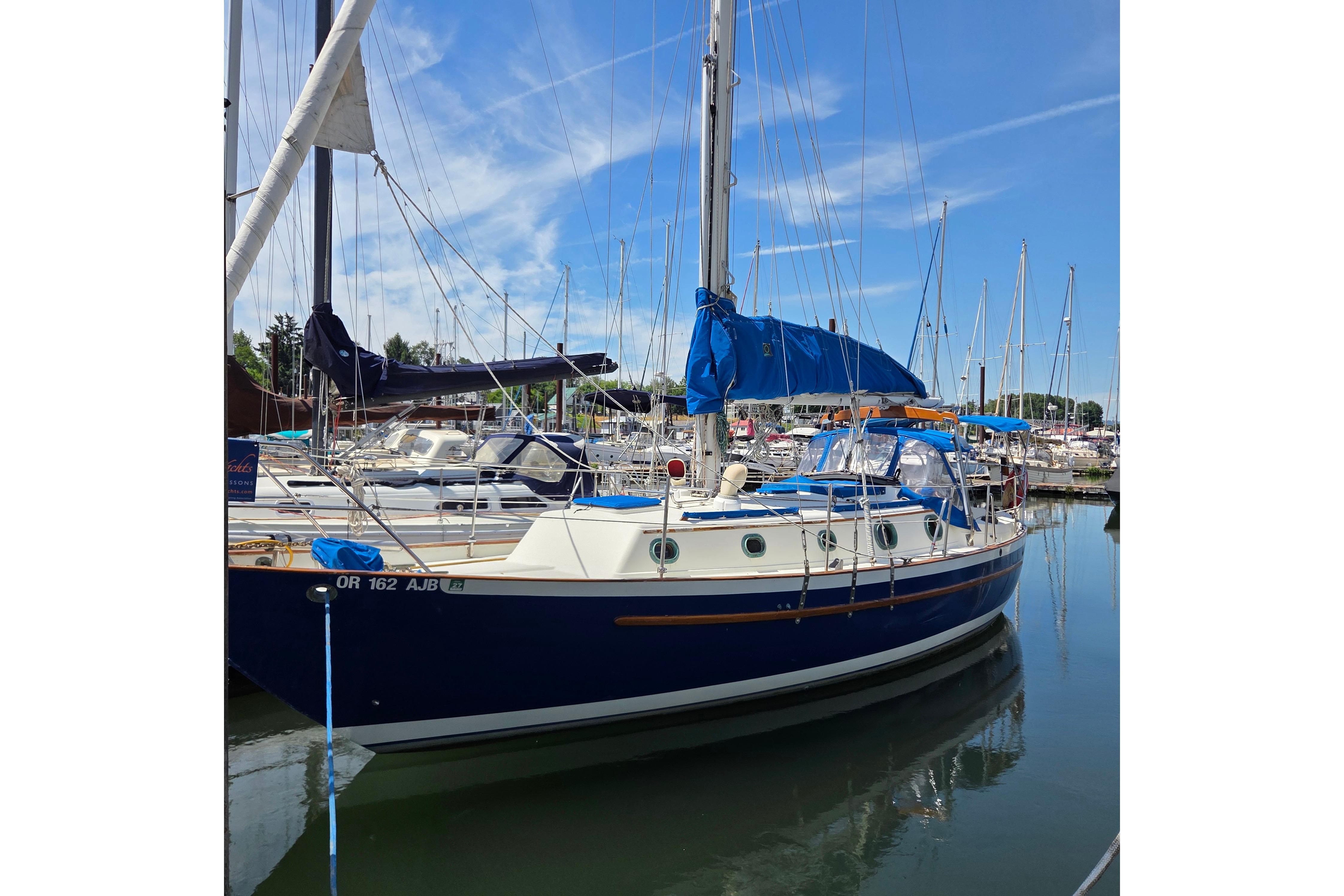 1983 Pacific Seacraft 34 sailboat docked in a marina under a clear blue sky.