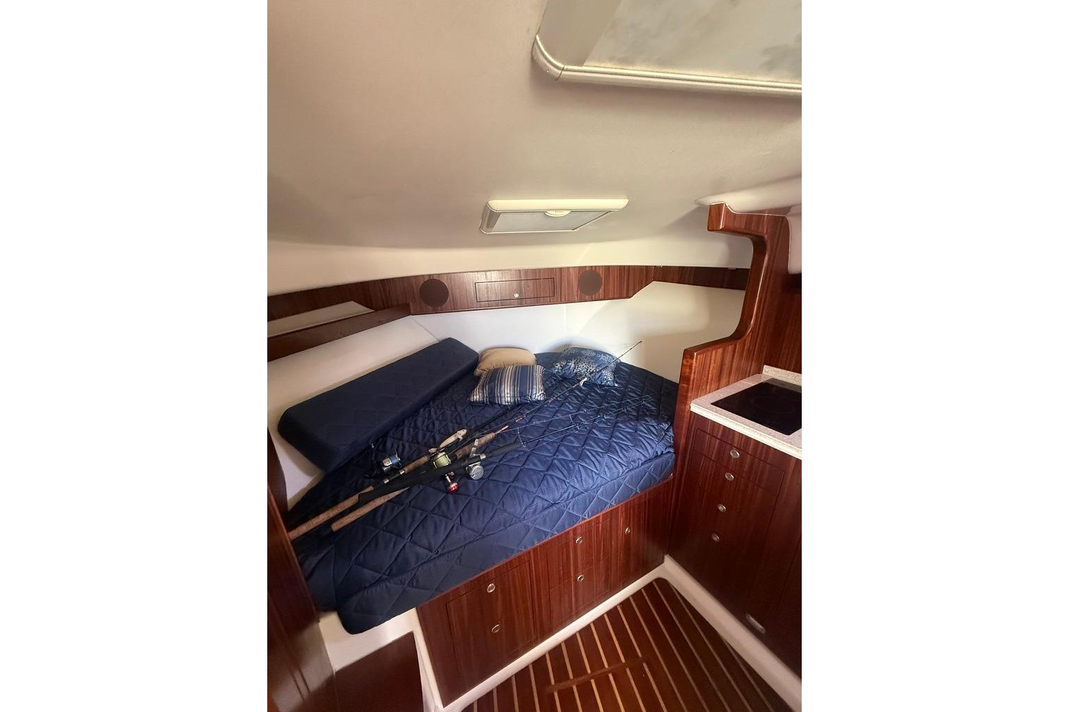 2010 Pursuit OS 375 Offshore cabin with bed, fishing rods, and wooden cabinetry.