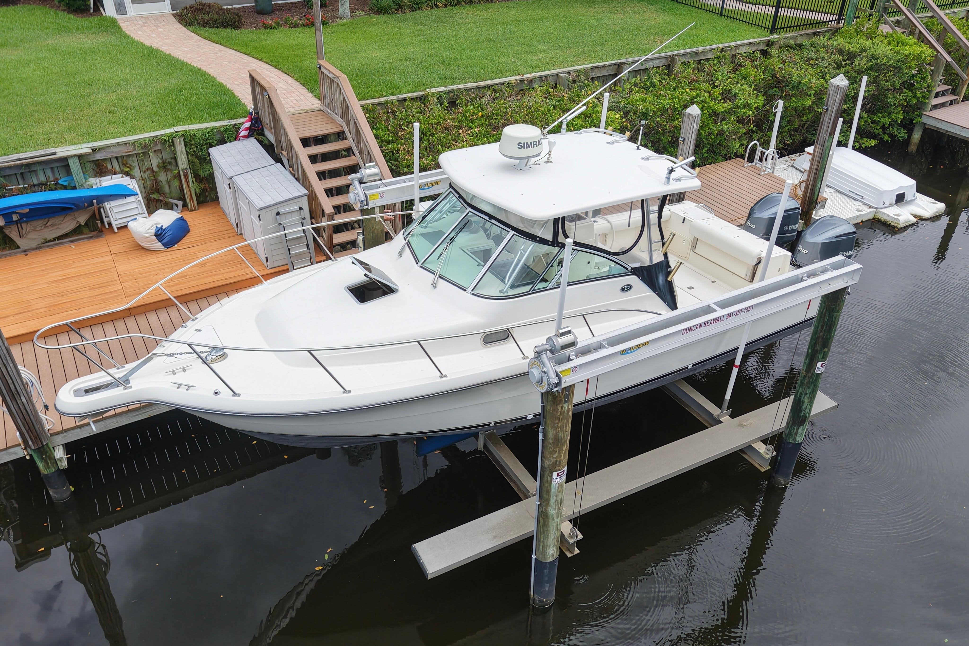 2005 Pursuit 3070 Offshore boat docked on a lift, near a wooden deck and green lawn.