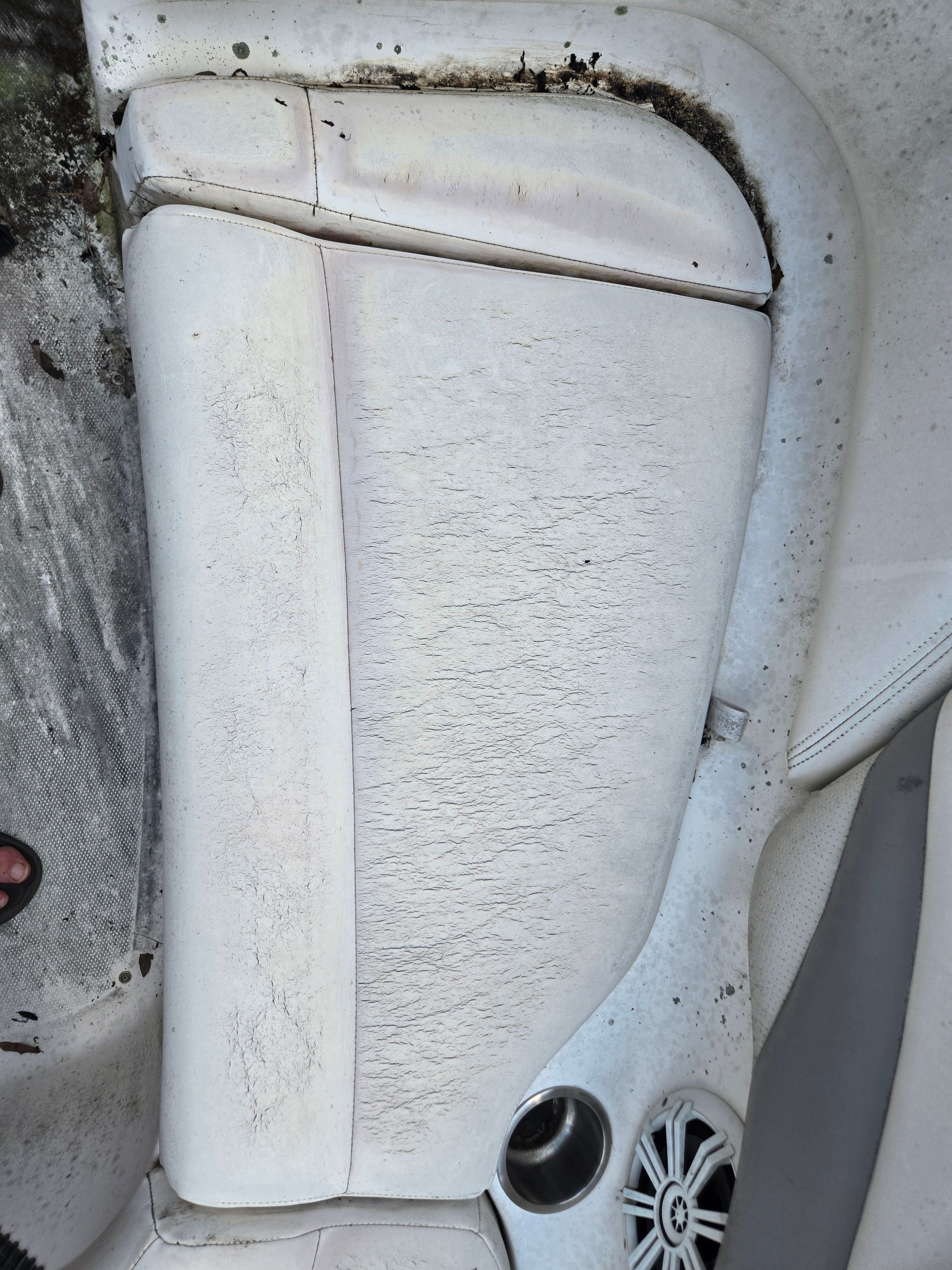 A worn white seat in a boat with a speaker and cup holder.