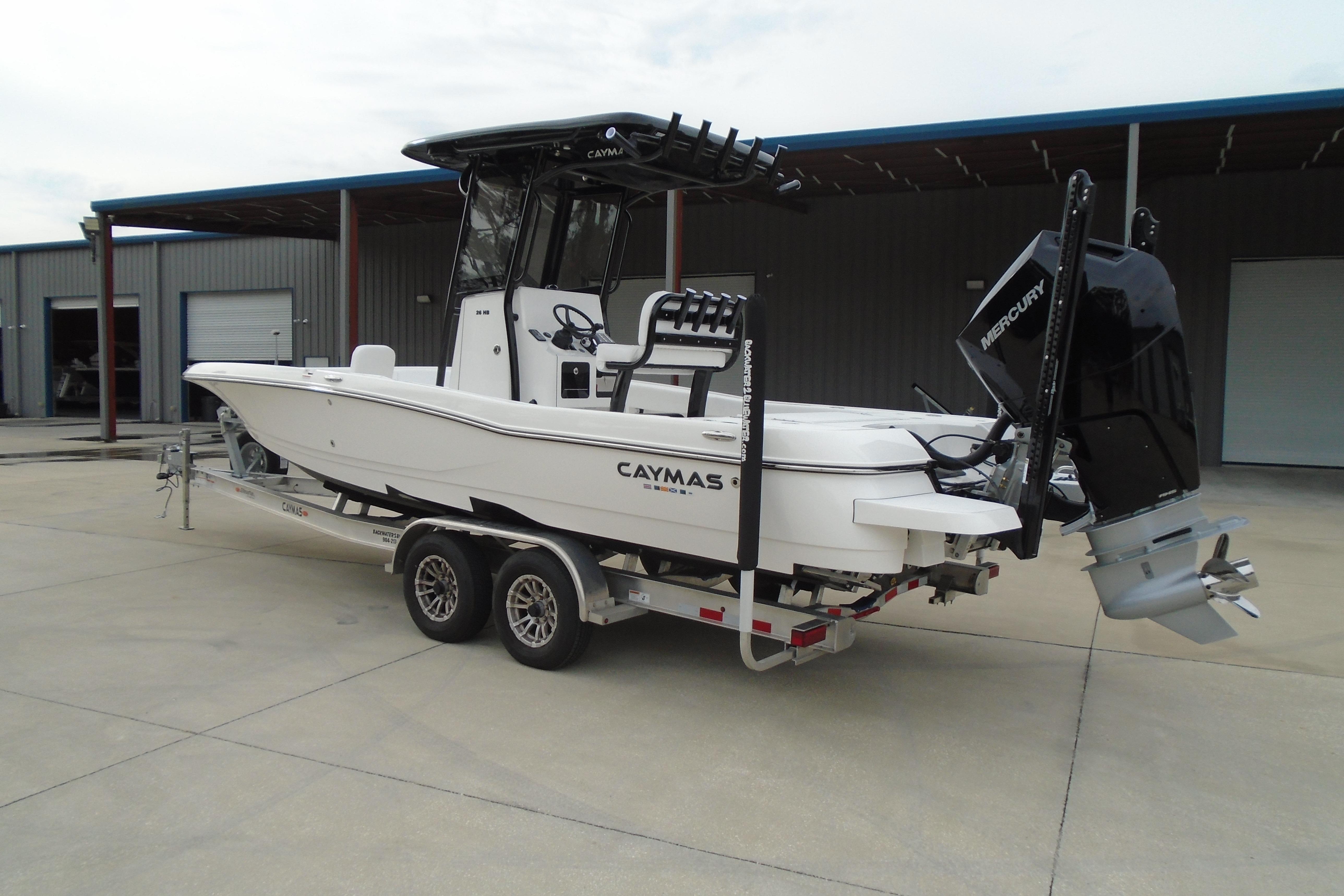 2026 Caymas 26 HB boat on trailer with Mercury engine, parked outside a warehouse.