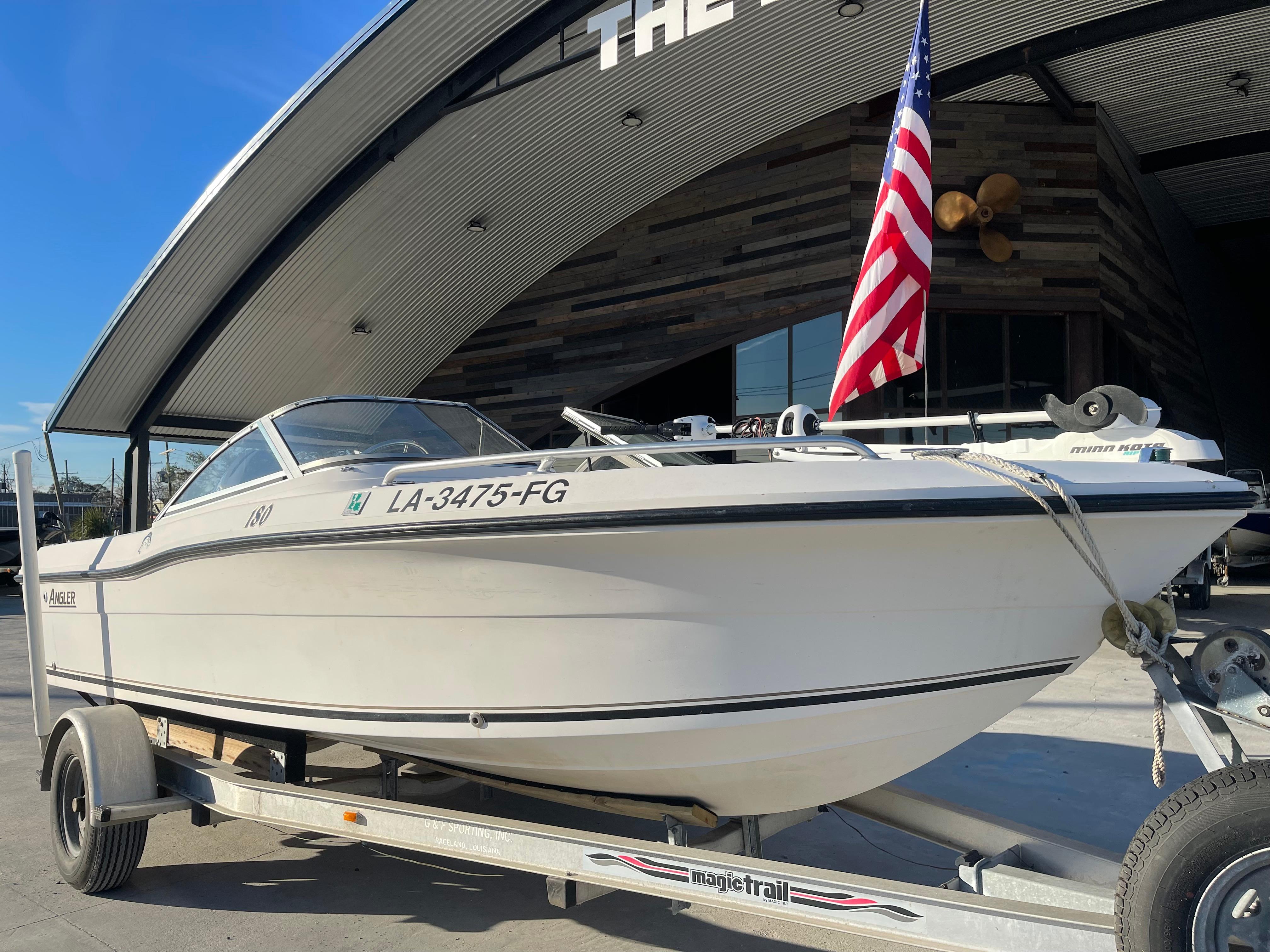 2002 Angler 18 DC boat on trailer with American flag, parked outside a modern building.