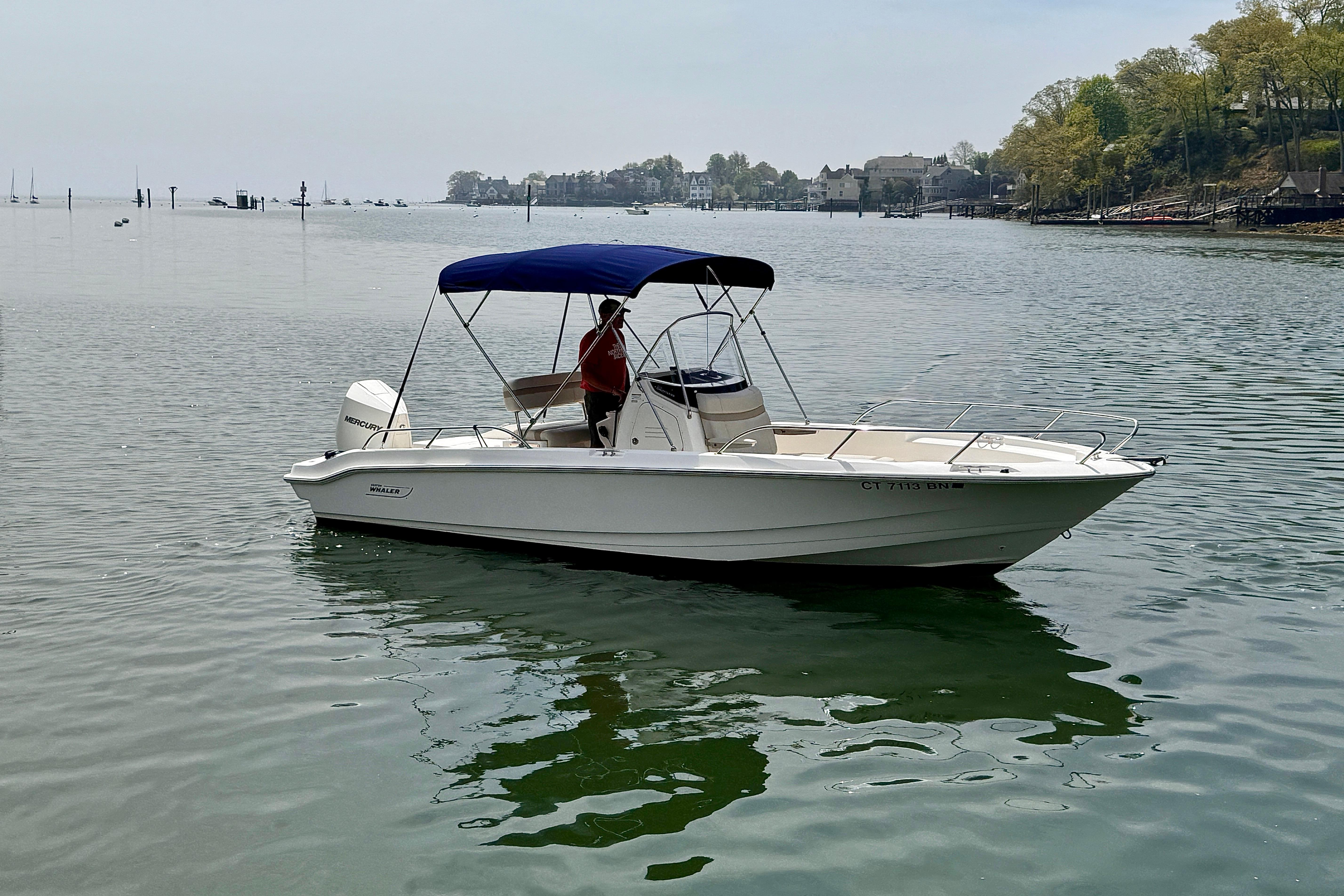 2022 Boston Whaler 220 Dauntless boat on calm water with blue canopy.