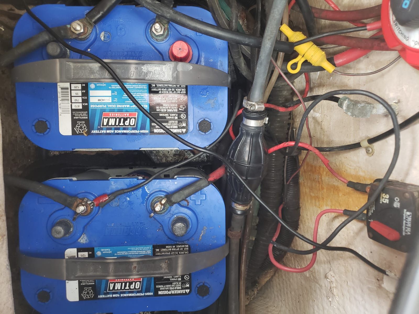 Two blue boat batteries are installed in a confined space, surrounded by cables and connectors.