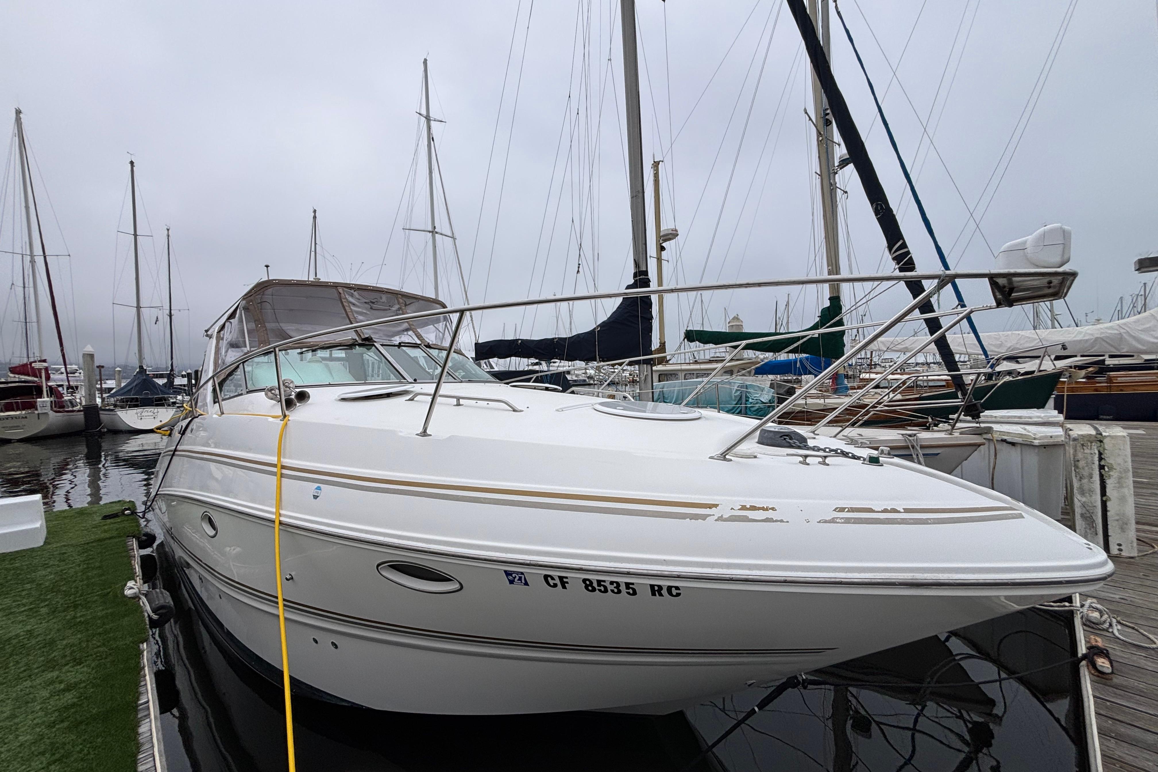 2004 Larson 310 boat docked at marina, surrounded by sailboats on a cloudy day.