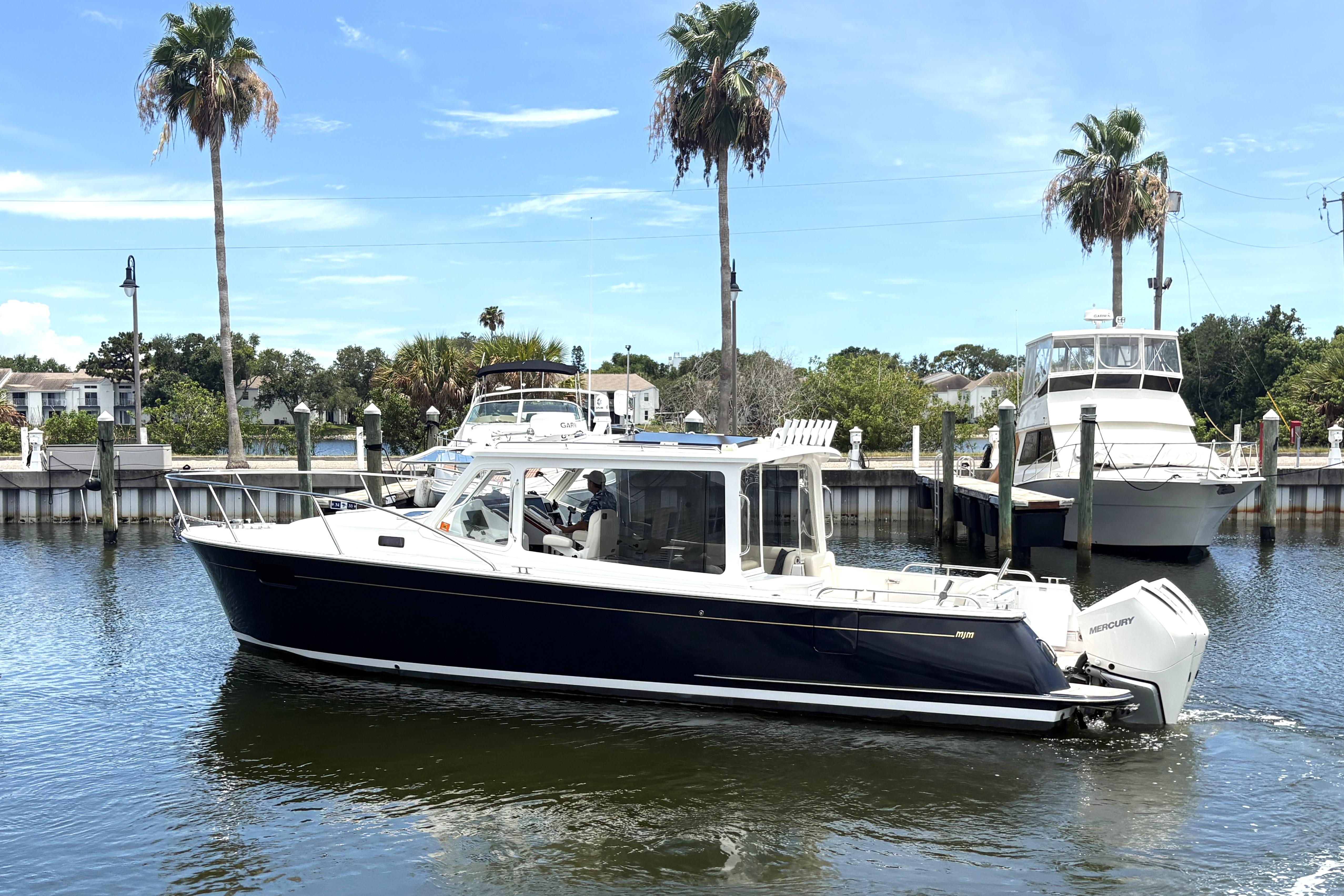 2024 MJM 35z boat docked in a marina with palm trees and clear skies.