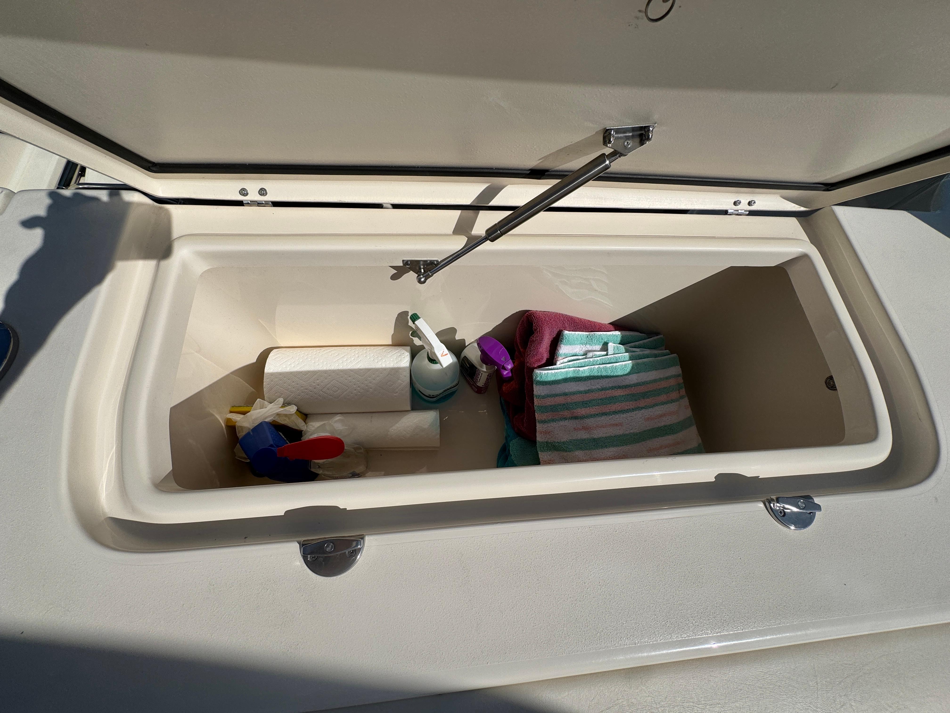Open storage compartment on 2019 Grady-White Freedom 307 boat with cleaning supplies and towels.