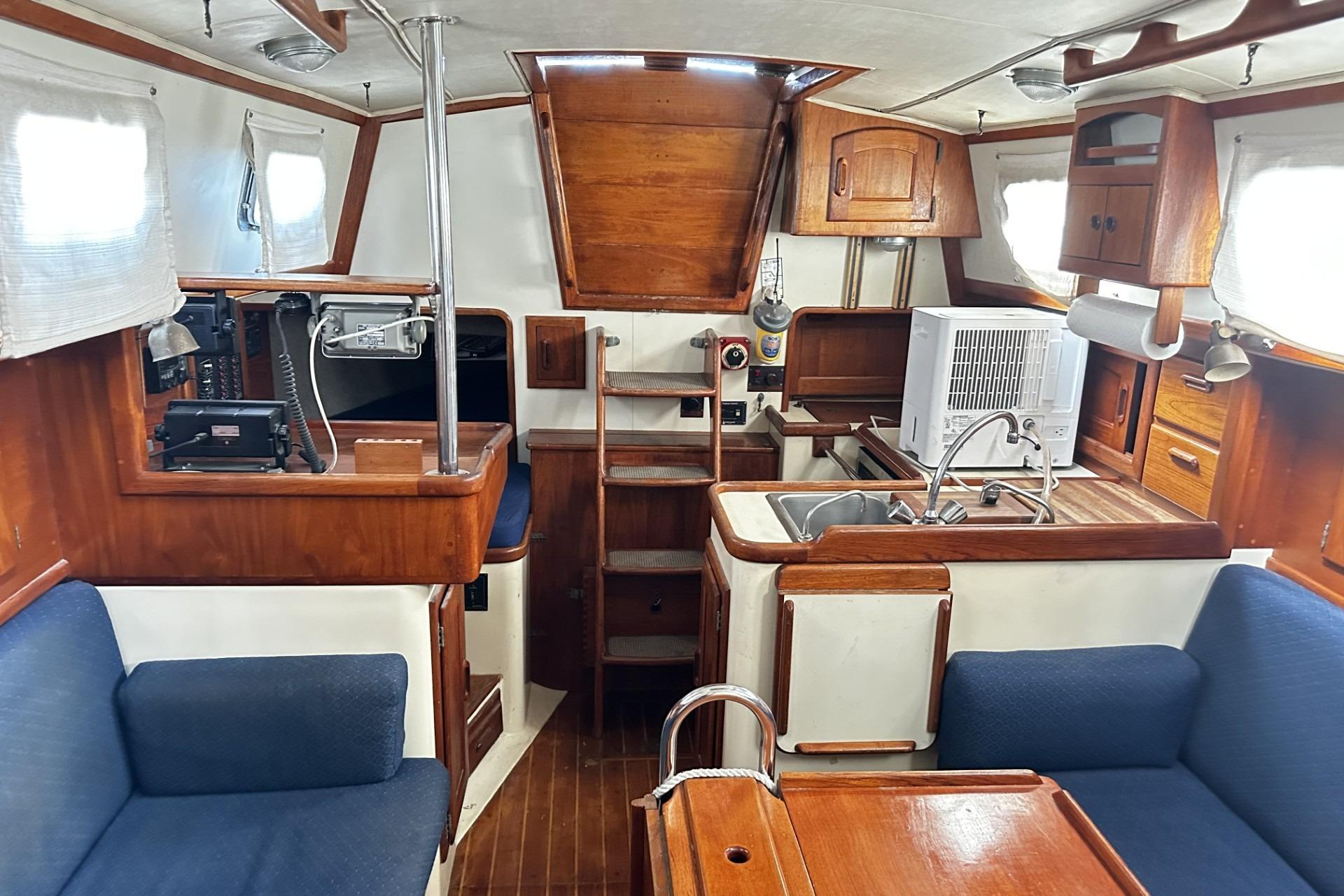 Interior of a 1990 Pacific Seacraft 34 sailboat with wooden cabinetry and blue seating.