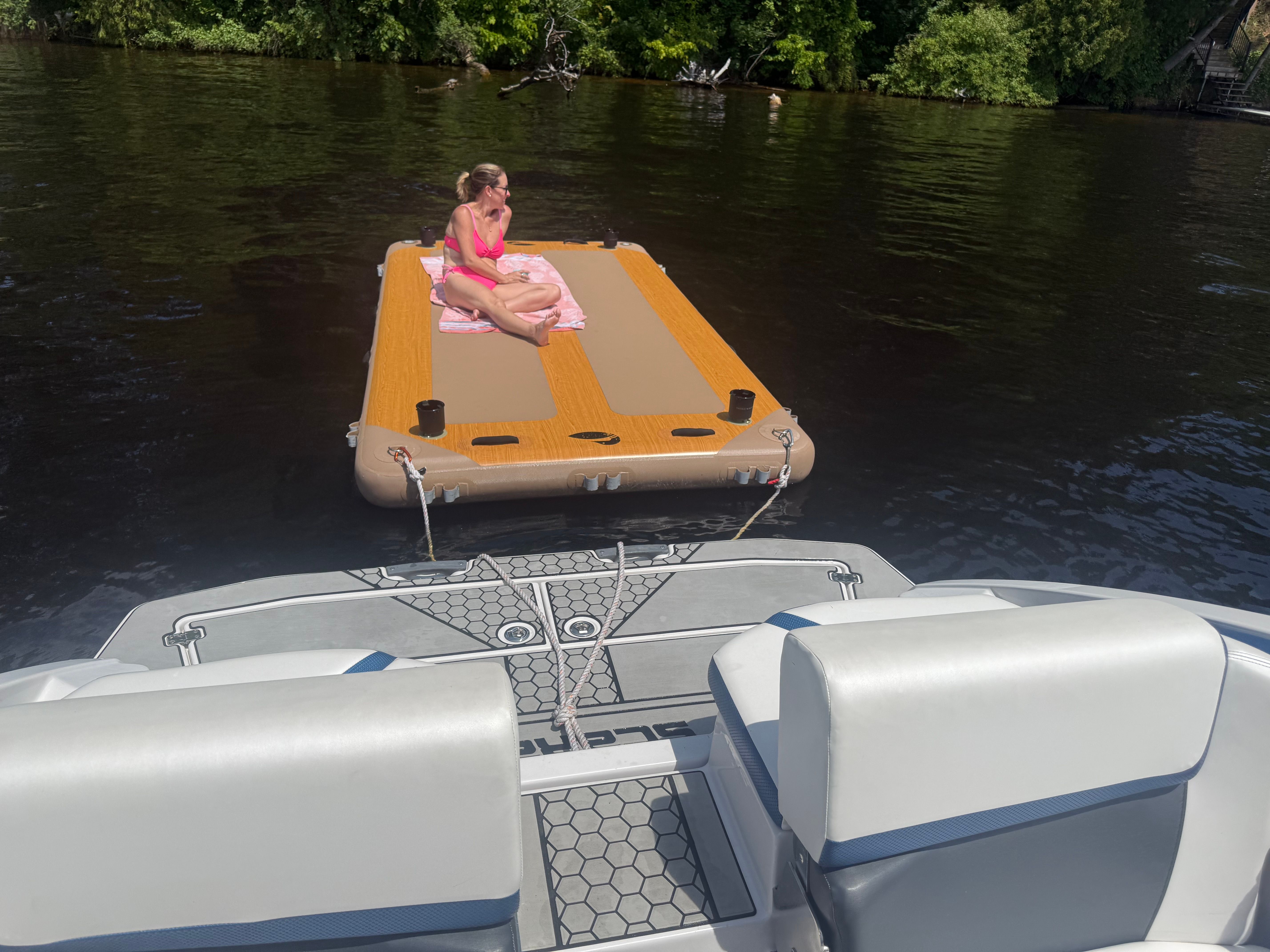 Woman relaxing on a floating platform behind a Scarab 255 HOI boat on a calm river.