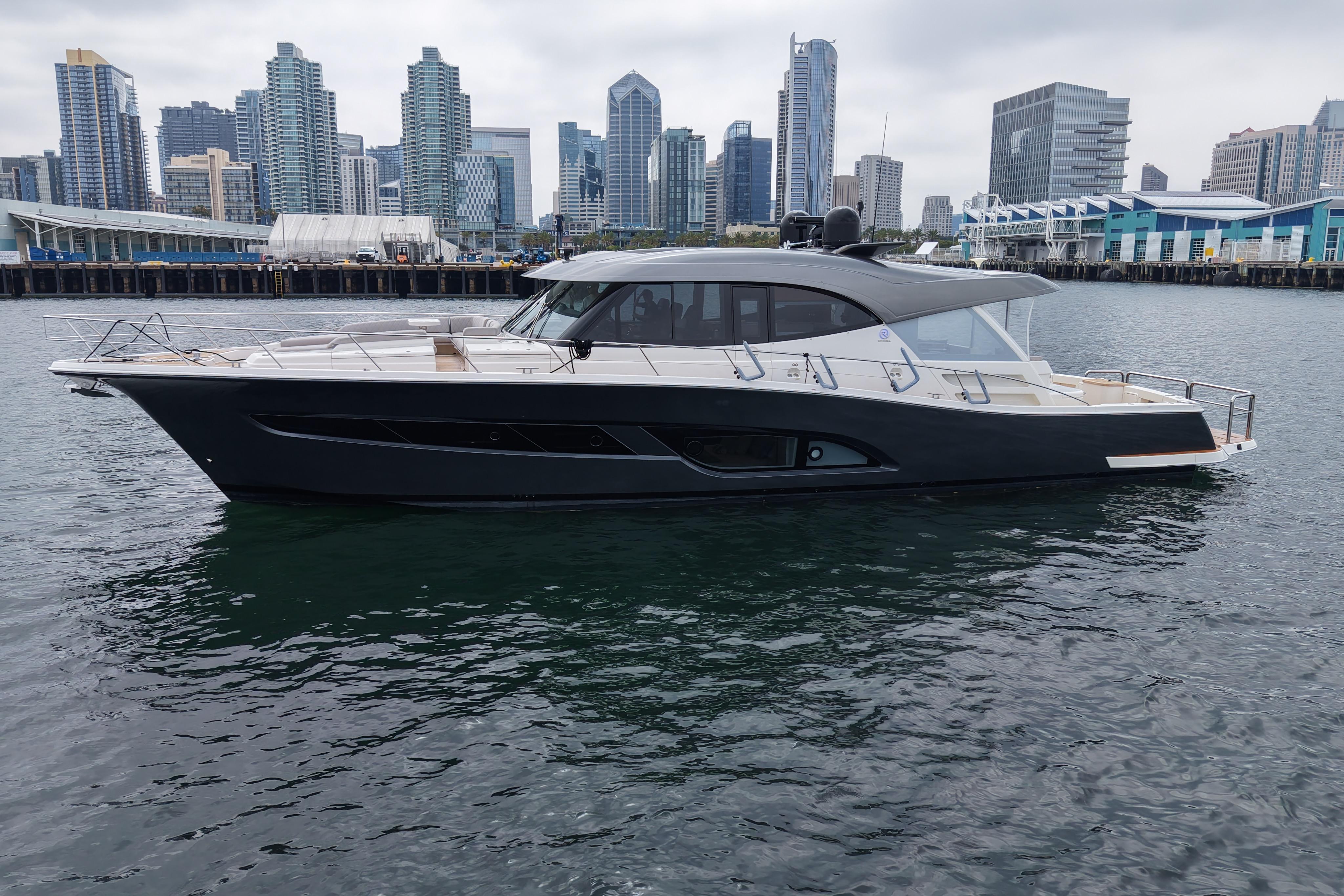 2023 Riviera 645 SUV yacht docked in urban harbor with city skyline backdrop.