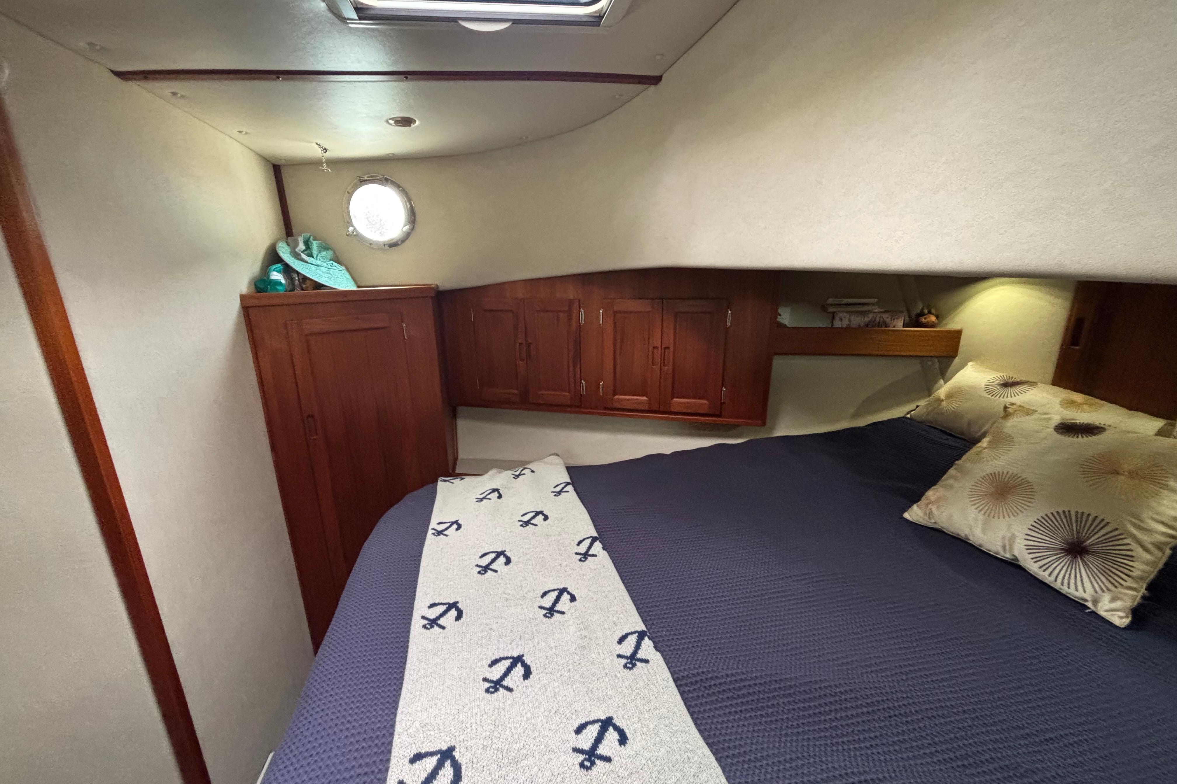 Cozy cabin interior of 2004 Nordic Tug 37 with nautical-themed bedding and wooden cabinetry.