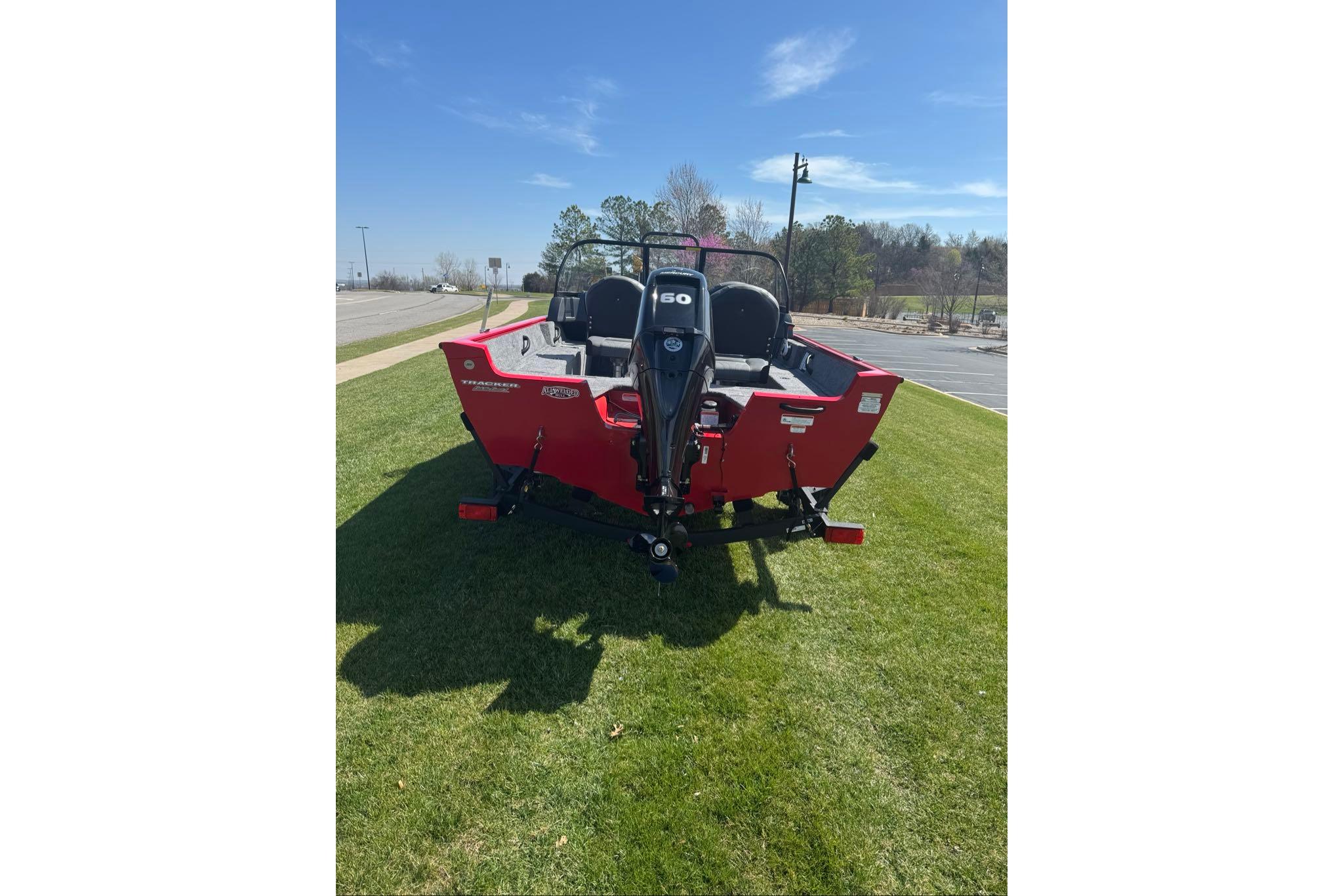 2026 Tracker Pro Guide V-16 WT boat, red exterior, parked on grass under clear sky.