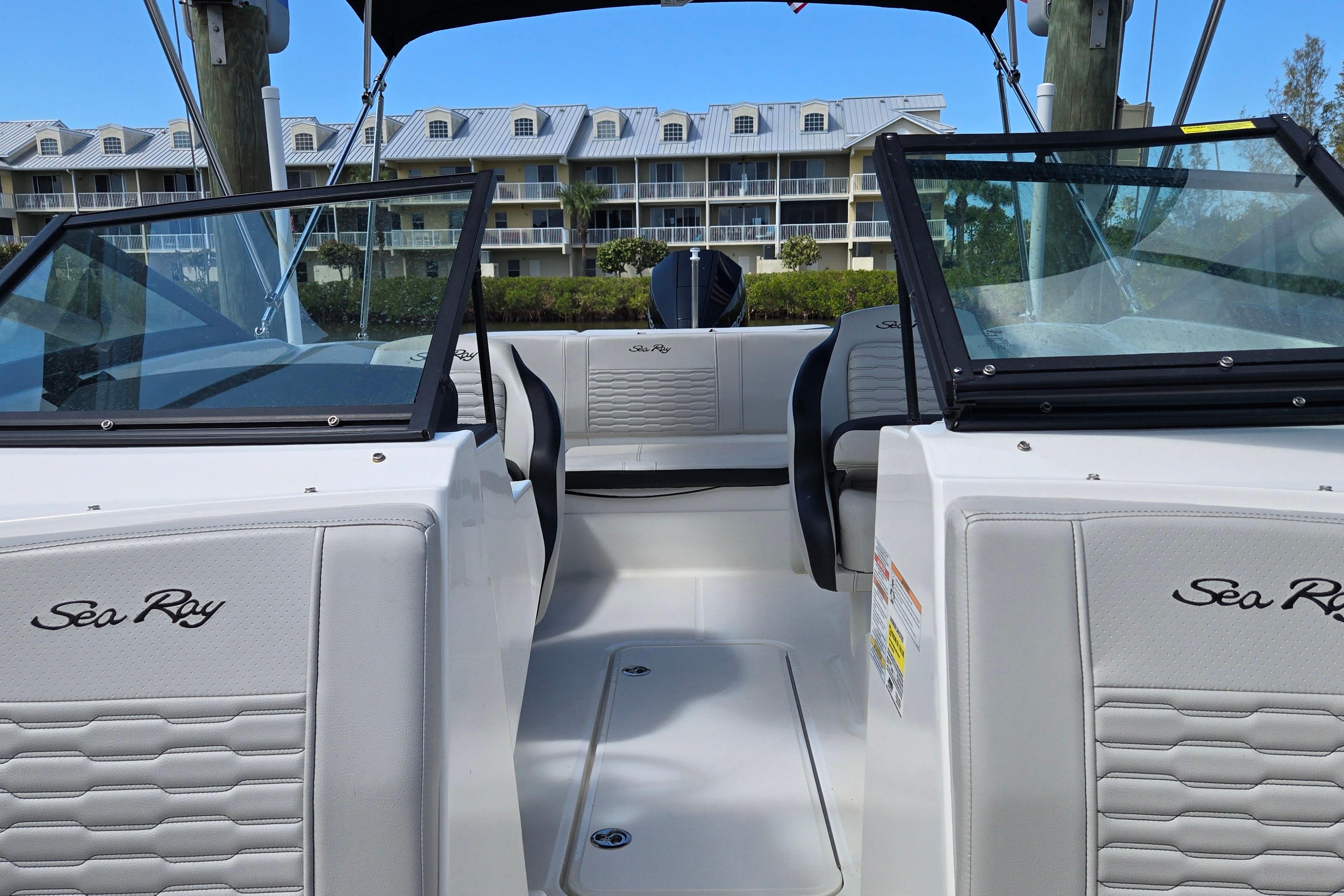 2023 Sea Ray SPX 210 boat interior with modern seating and windshield, docked near buildings.