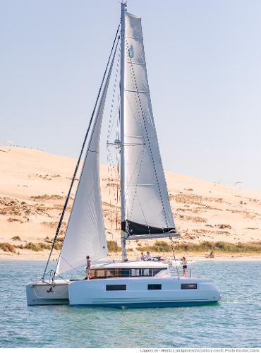 2025 Lagoon 46 ICONIC catamaran sailing near sandy shore under clear blue sky.
