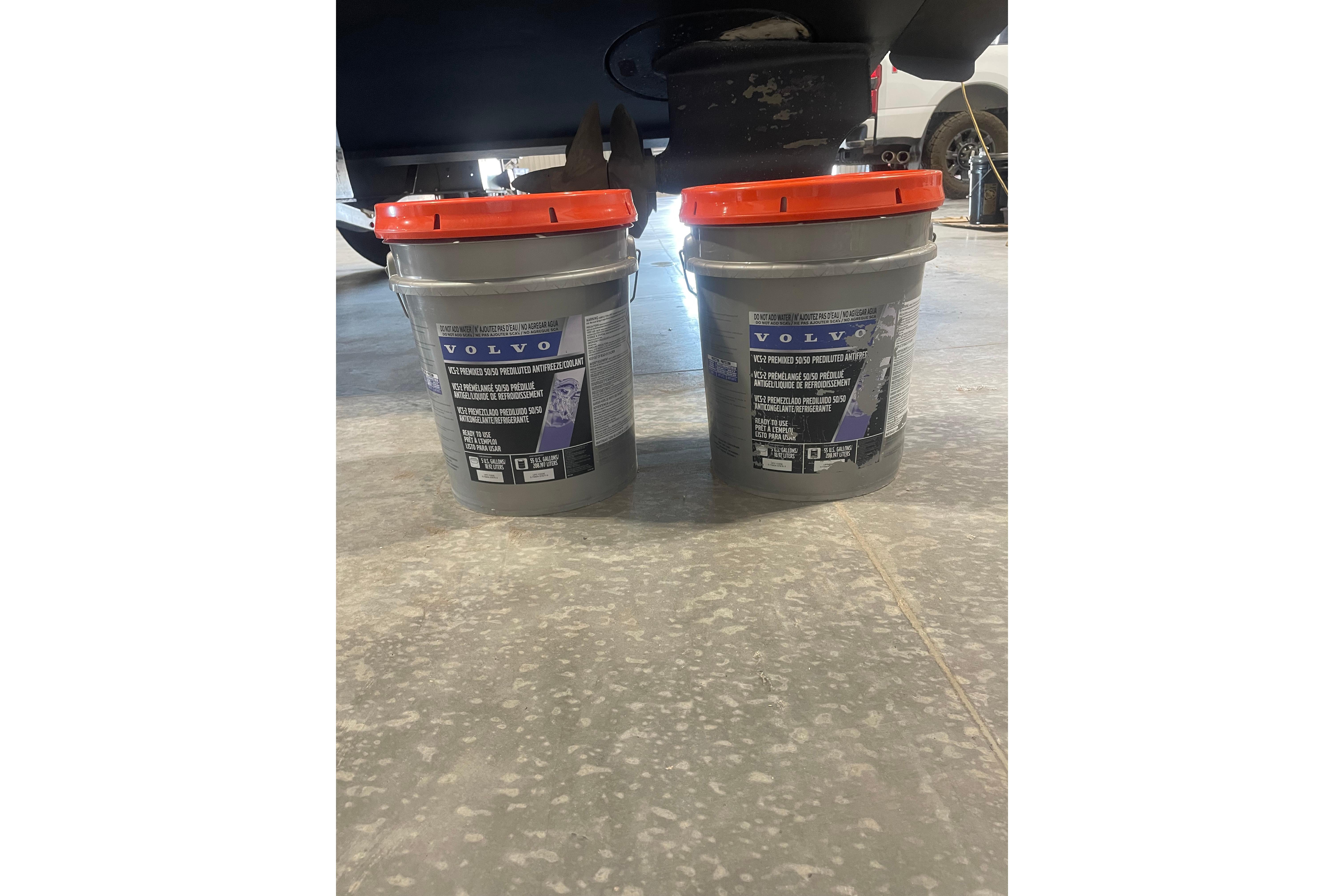 Two Volvo antifreeze buckets on a garage floor near a 2011 Cruisers Yachts 390 Sports Coupe.