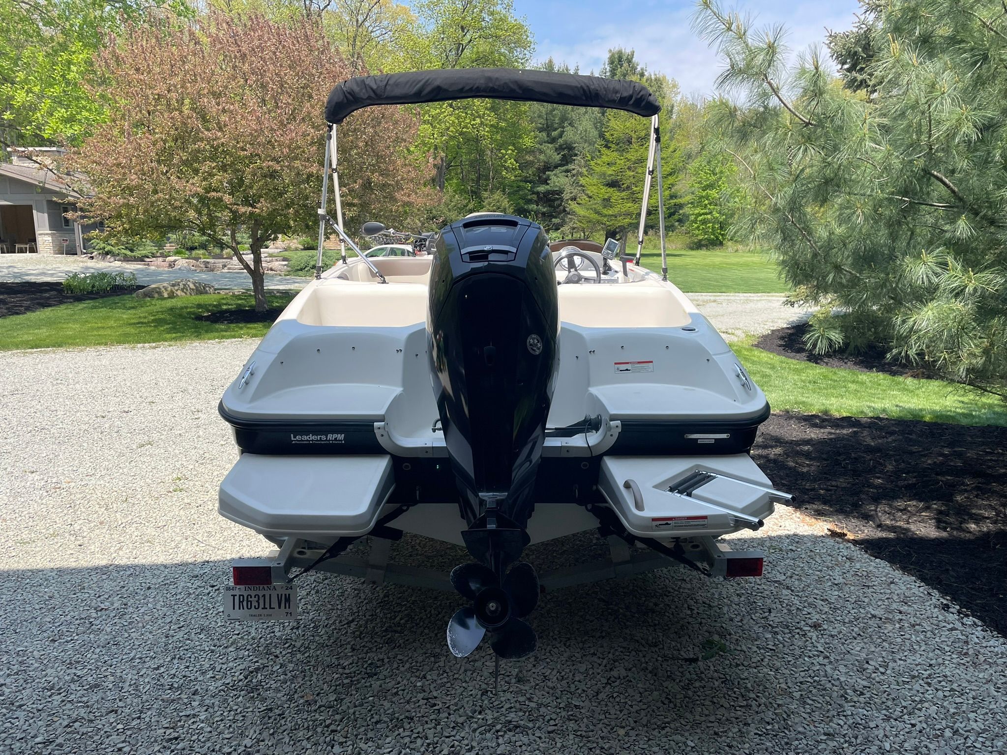 2018 Bayliner 160 Bowrider with outboard motor, parked on a gravel path, surrounded by trees.