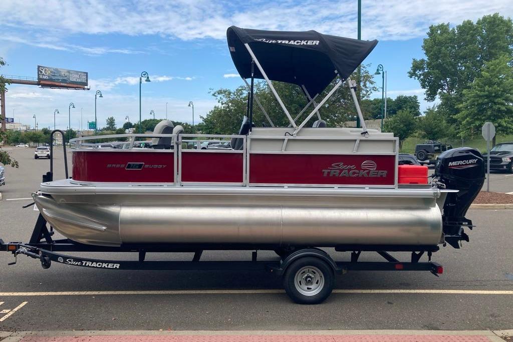 2026 Sun Tracker Bass Buggy 16 XL Select pontoon boat on trailer, parked outdoors.