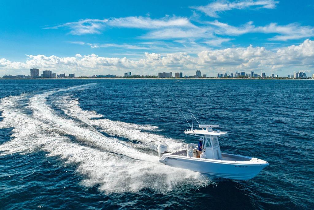 2024 Reef Runner 230 Open boat cruising on ocean with city skyline in background.