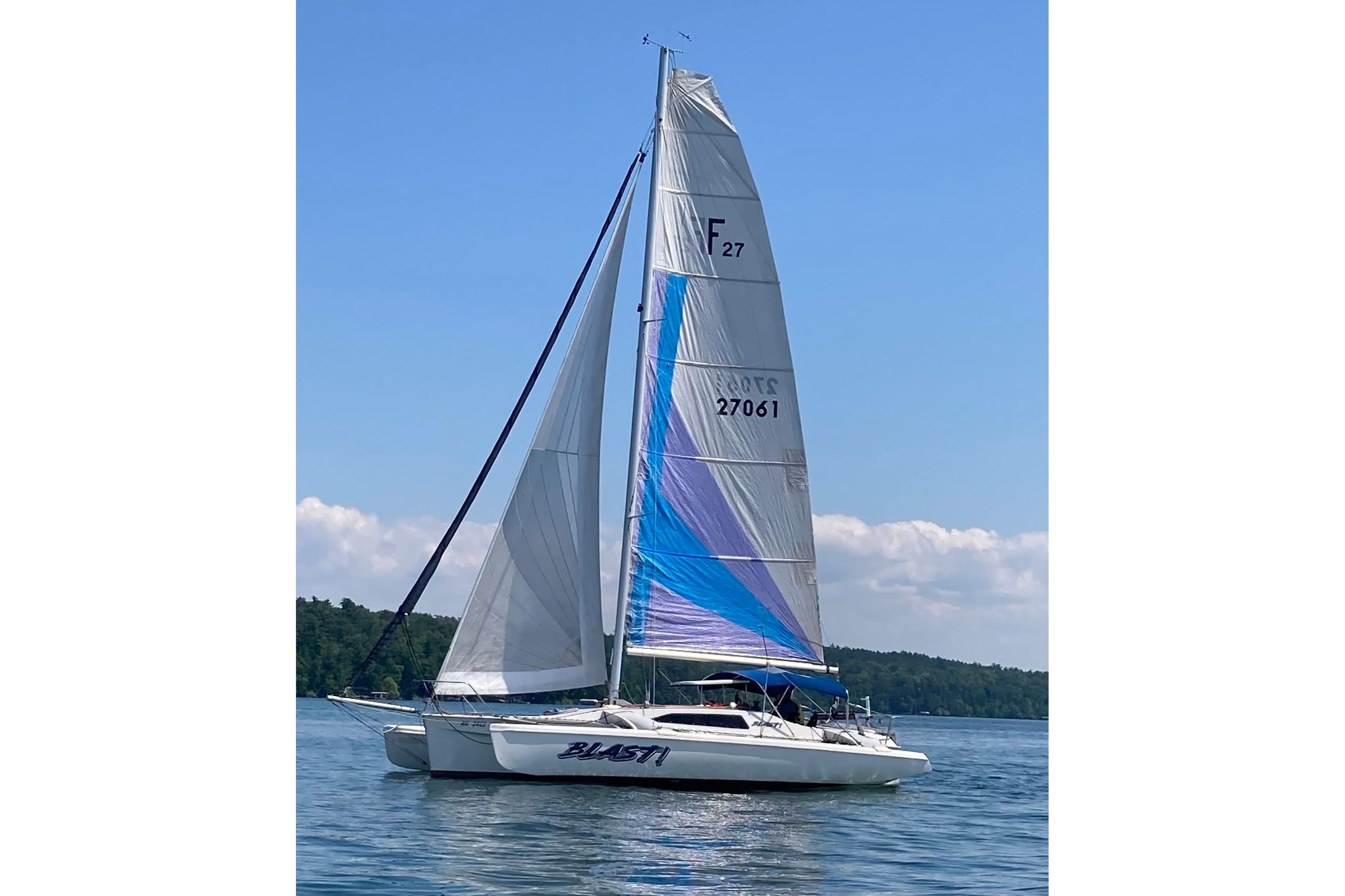 Sailing Corsair F-27 trimaran from 1993 on a calm lake under clear blue skies.
