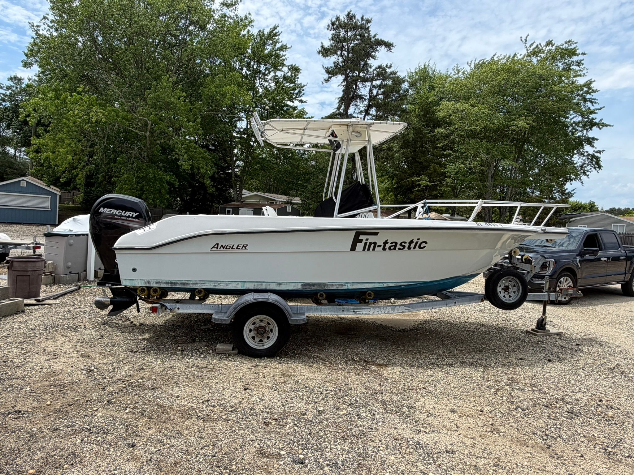 An Angler boat on a trailer, surrounded by trees and vehicles.