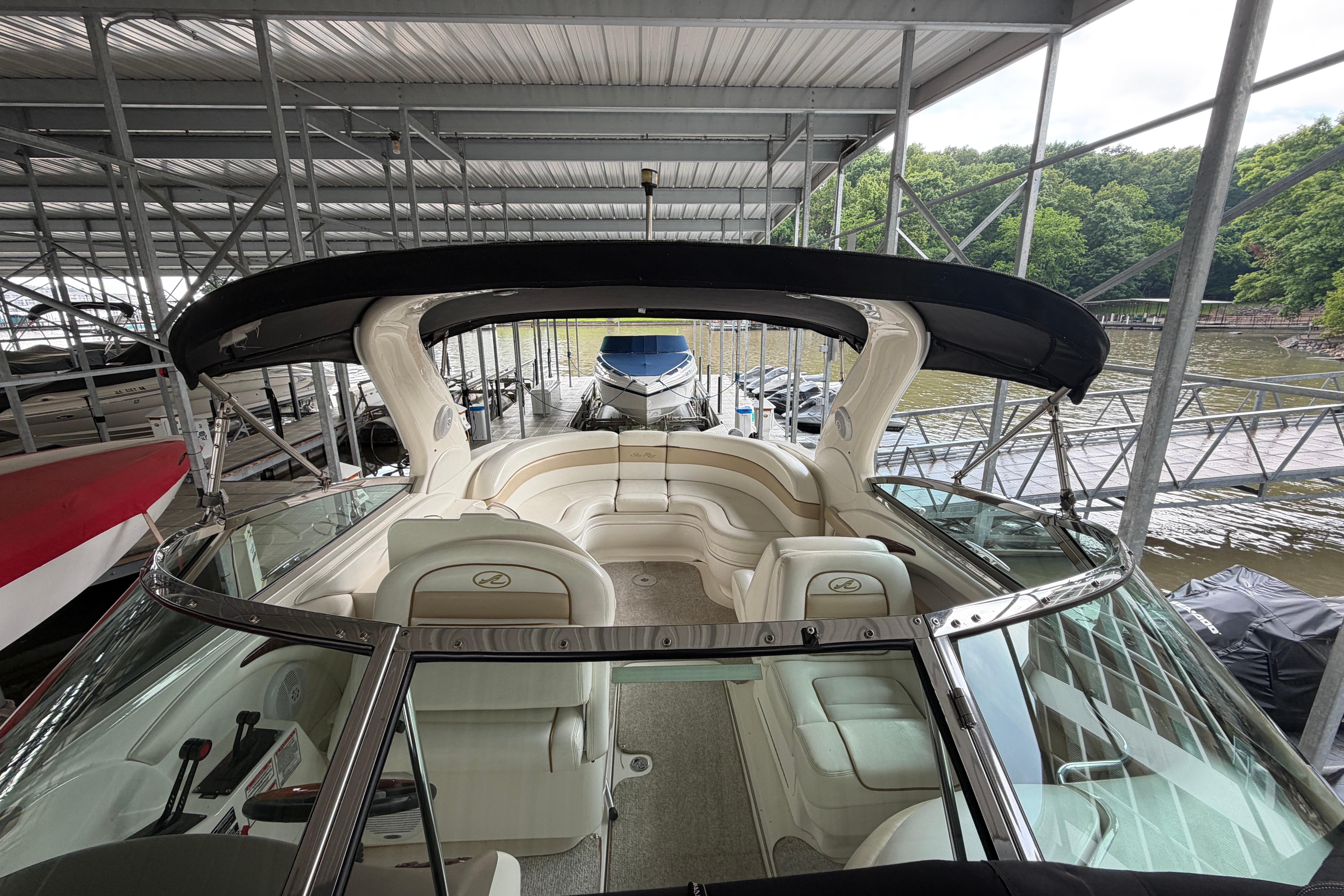 2003 Sea Ray 290 Bowrider docked under a covered marina with lush greenery.