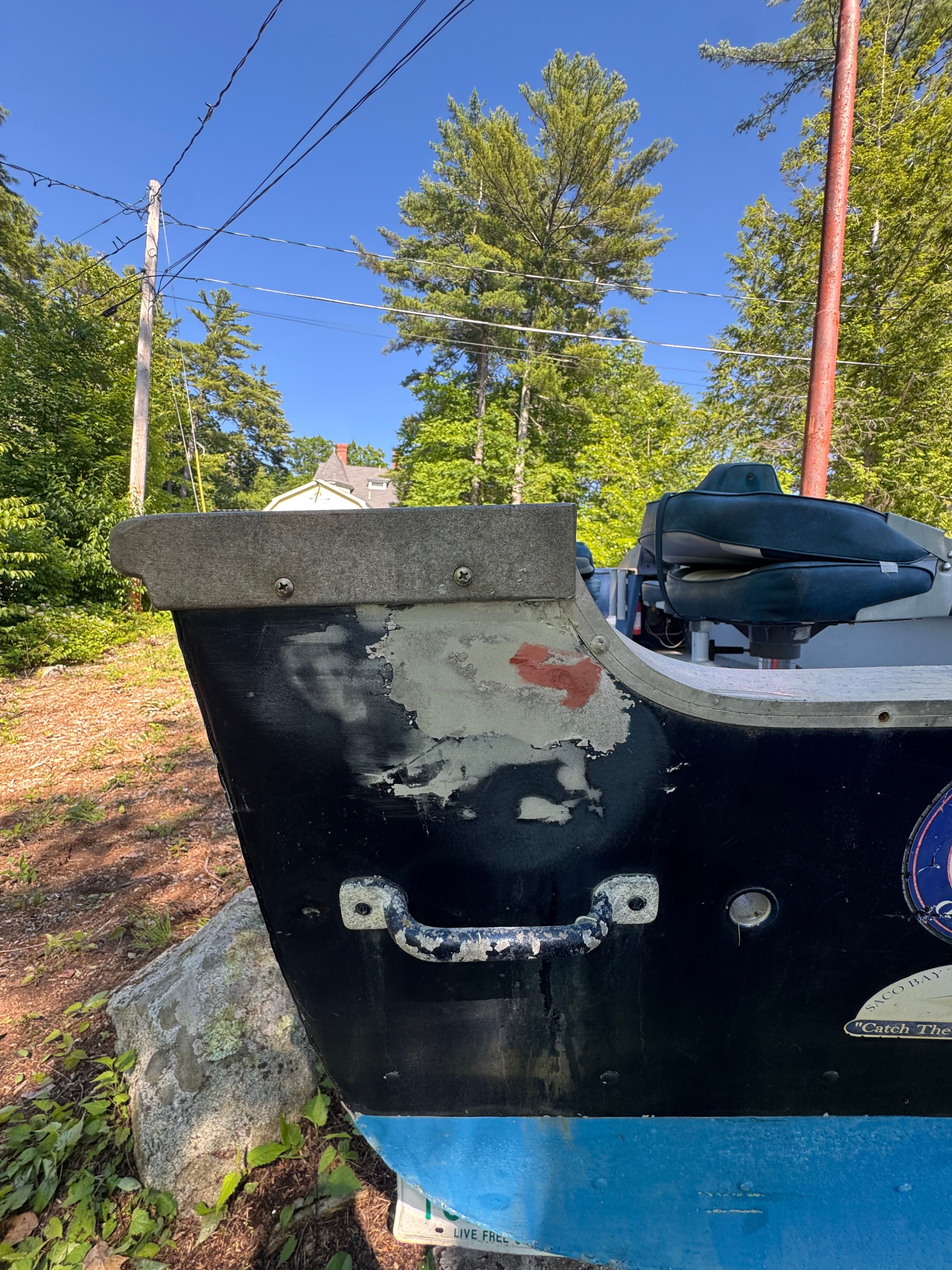 A damaged boat with a repaired area, surrounded by trees and power lines.