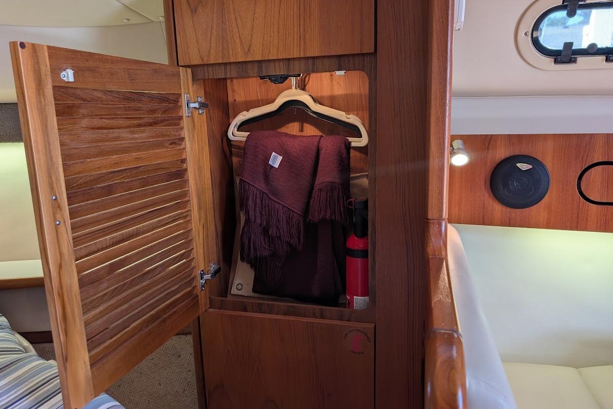 Wooden cabinet interior on a 2000 Pursuit 3400 Express boat, featuring a hanger and fire extinguisher.